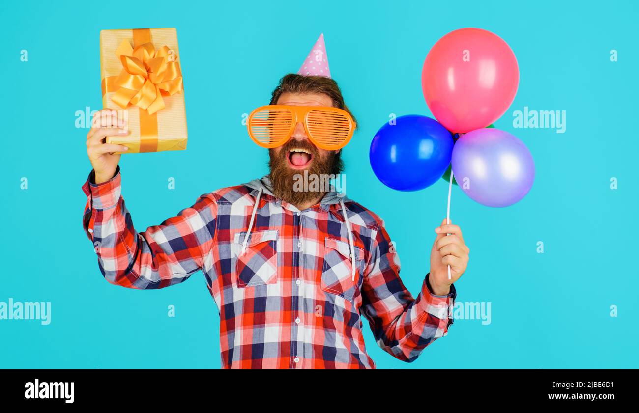 Konzept wird gefeiert. Alles Gute zum Geburtstag. Glücklicher Mann in lustigen Partybrillen mit Geschenk-Box und Ballons. Stockfoto