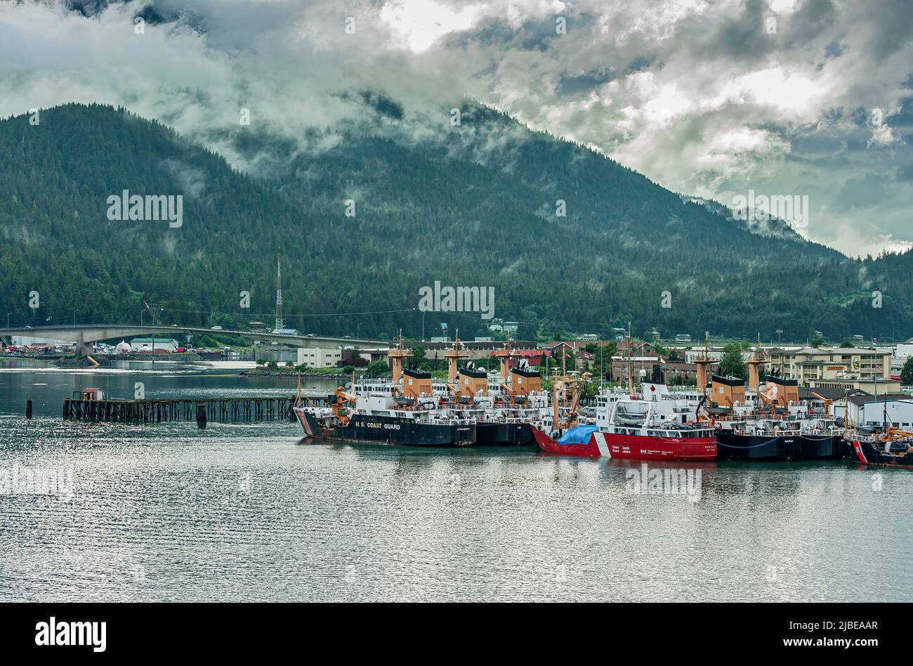 Juneau, Alaska, USA - 19. Juli 2011: Rote und schwarze Küstenschutzschiffe dockten in einer Gruppe im Hafen an. Douglas Brücke hinten unter Kiefernwald bedeckend Moun Stockfoto