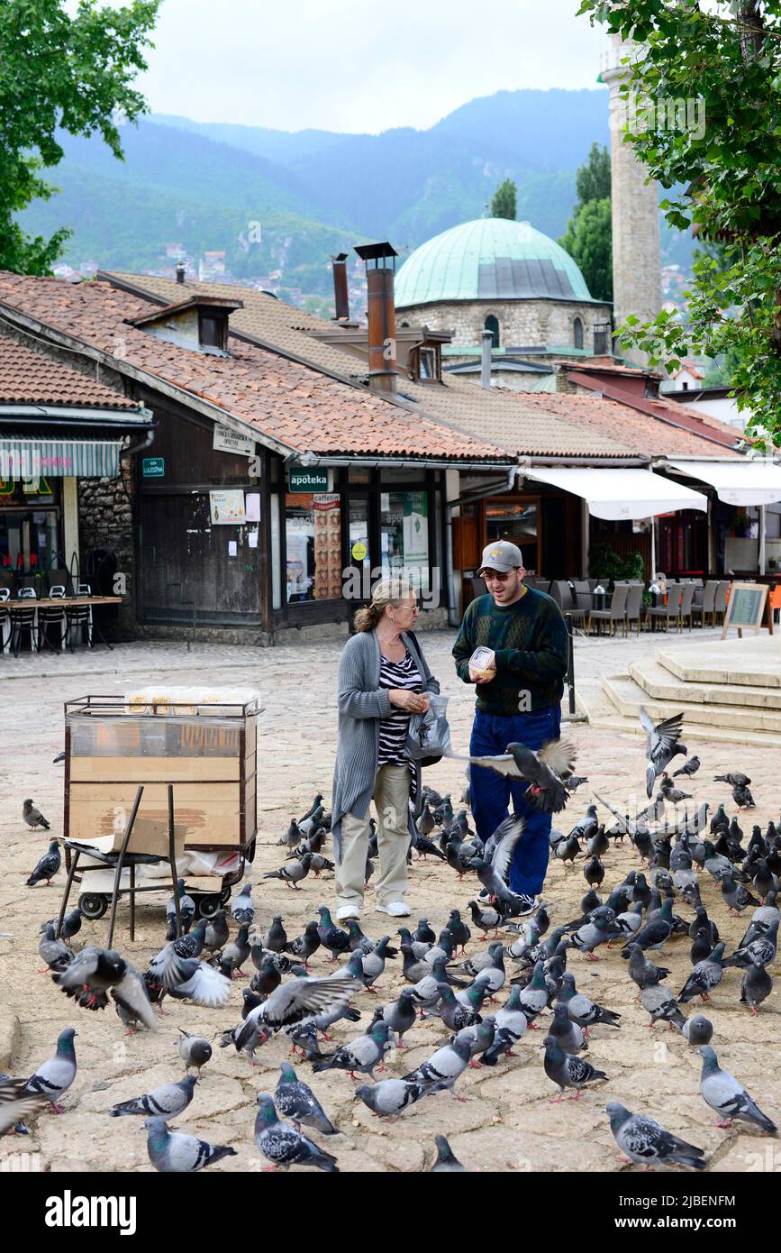 Ein bosnisches Paar füttert Tauben auf dem Baščaršija-Marktplatz in Sarajevo, Bosnien und Herzegowina. Stockfoto