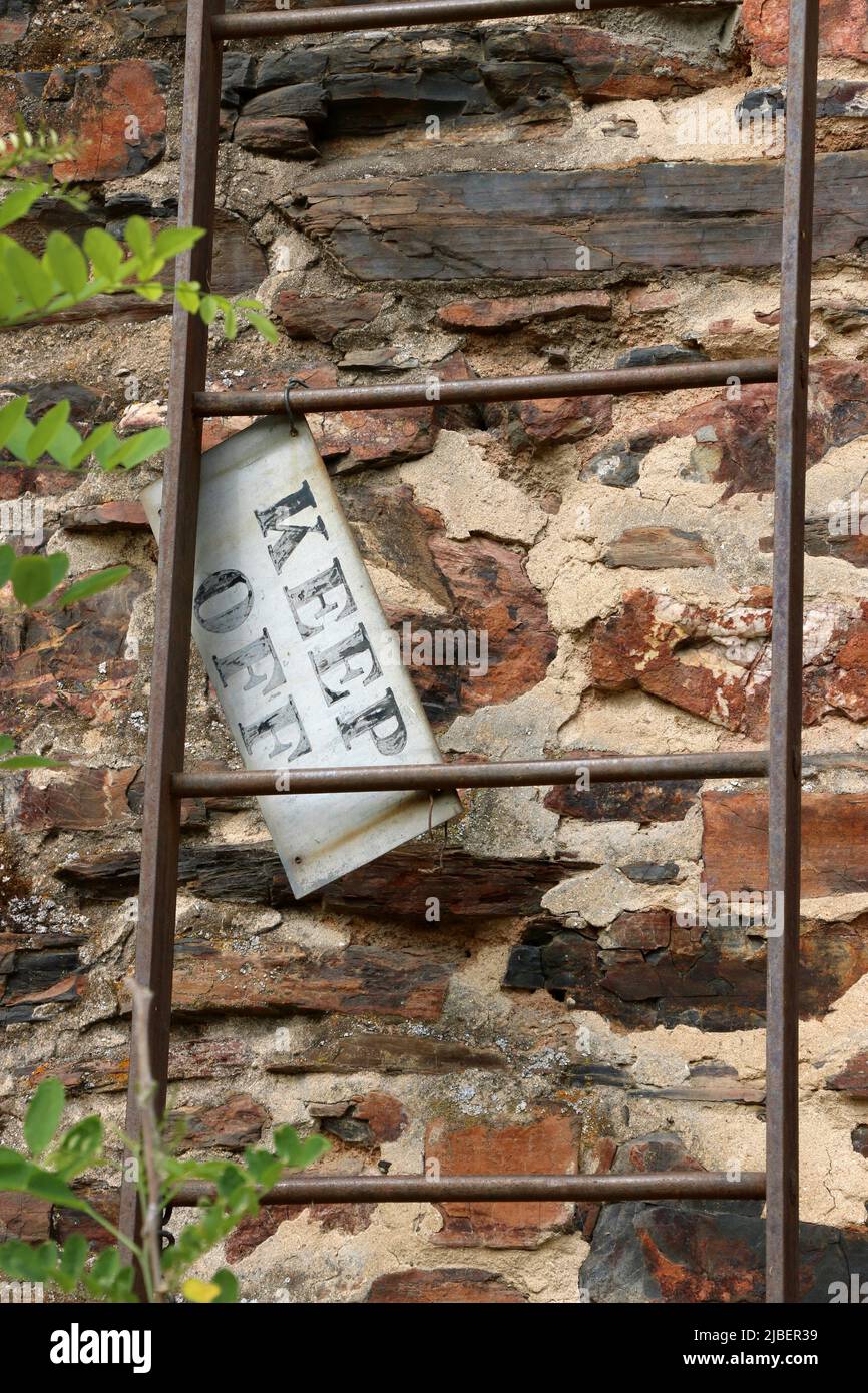 Das Schild „Keep Off“ hängt an einer verrosteten Leiter, die sich an einem verlassenen Ziegelgebäude lehnt. Stockfoto