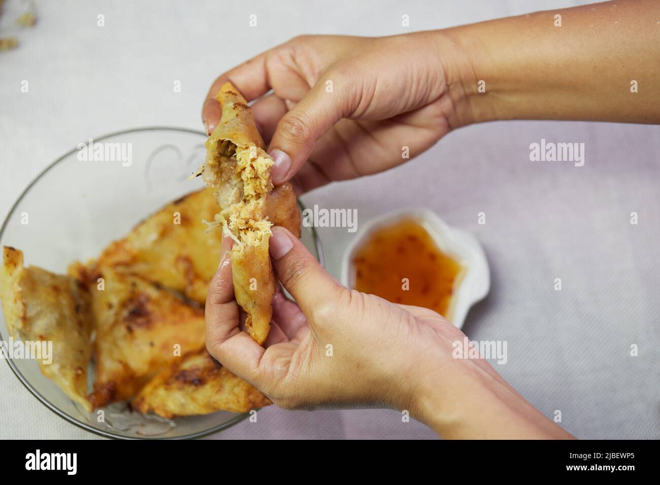 Frau Hand hält Samosa mit Sauce auf weißem Tischtuch Stockfoto