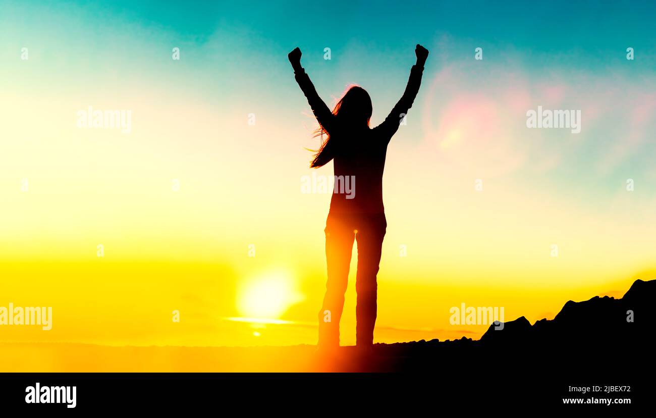 Glückliche Frau Silhouette mit Waffen für den Lebenserfolg feiert finanzielle Freiheit Frühpensionierung bei Sonnenuntergang glühen Sonne am Berggipfel. Wellness Stockfoto