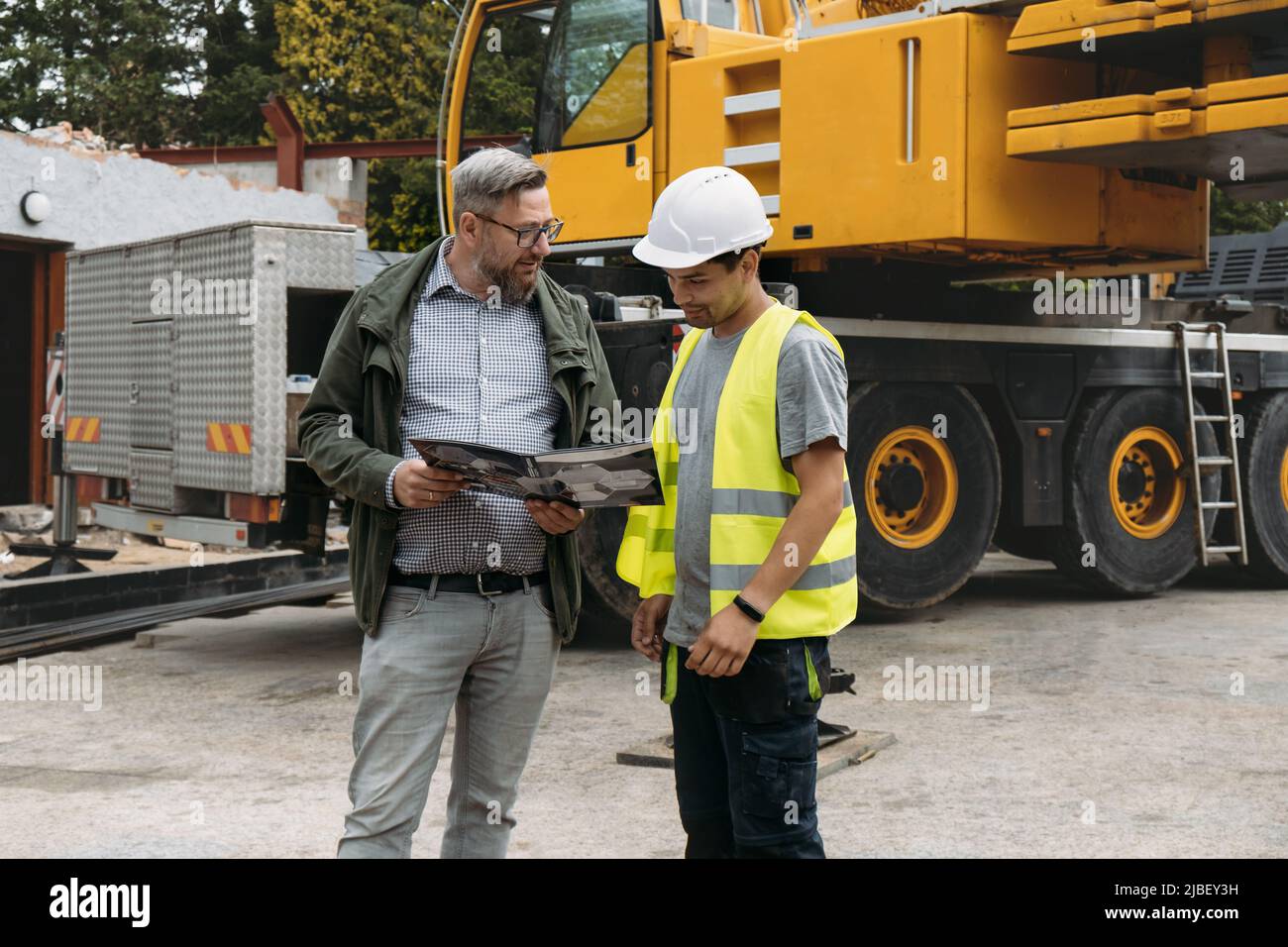 Vorarbeiter und Kunde oder Kunde stimmen über zukünftige Bauarbeiten auf der Baustelle überein. Architekt diskutiert Projekt mit dem Baumeister über Kranfahrzeug Stockfoto