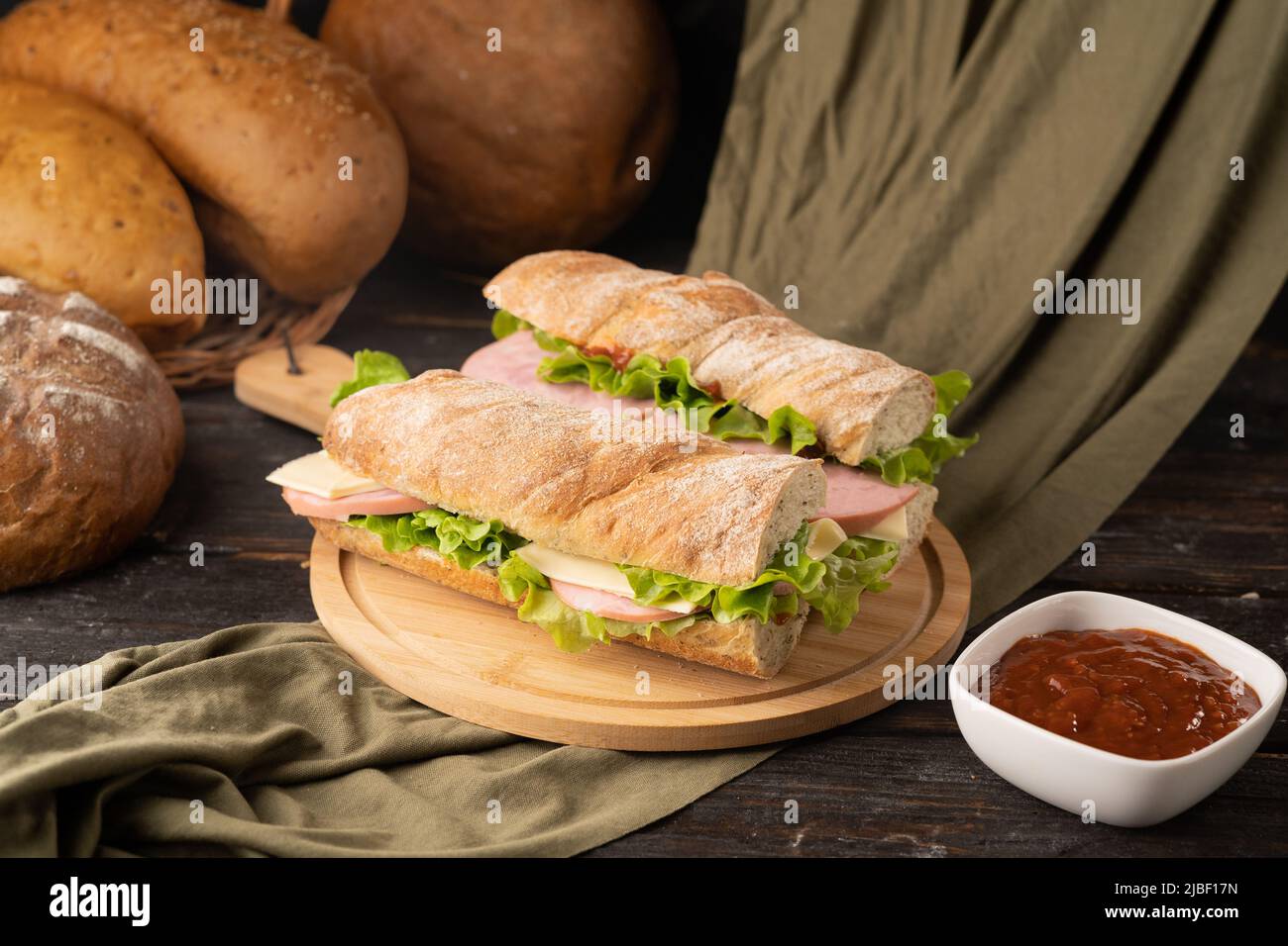 Köstliches Baguette-Sandwich mit Speck, Weichkäse, Tomaten und grünen Salatblättern auf einem Holzschneidebrett Stockfoto