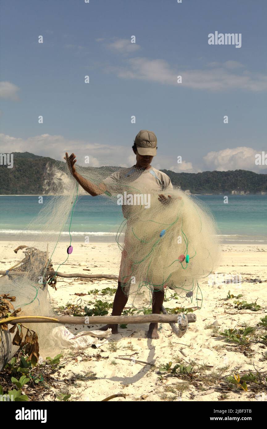 Ein Subsistenzfischer, der sein Fischernetz am Strand von Tarimbang in Tabung, East Sumba, East Nusa Tenggara, Indonesien, abrollt. Stockfoto