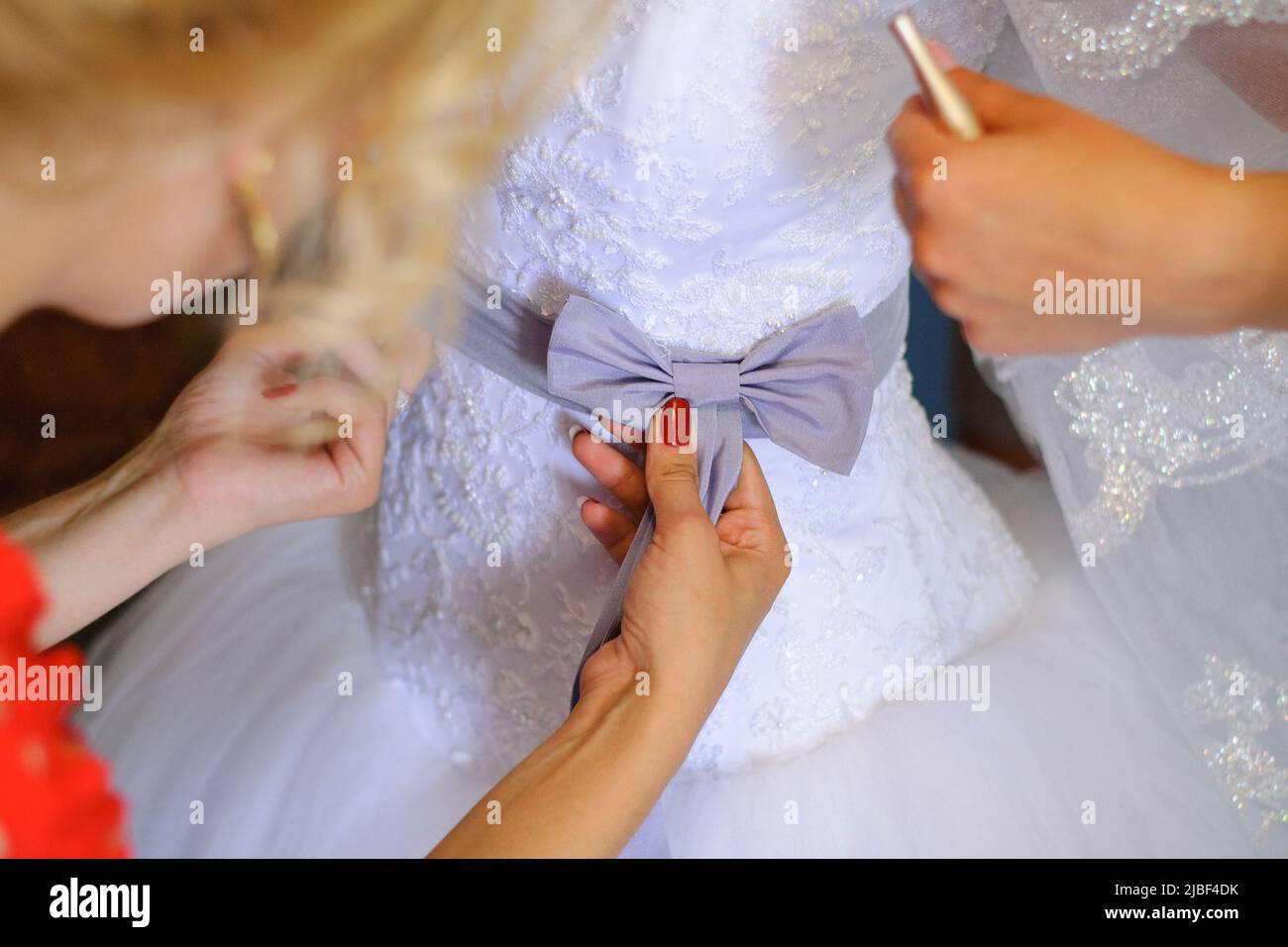 Brautjungfern helfen der Braut, ihr Hochzeitskleid anzuziehen Stockfoto