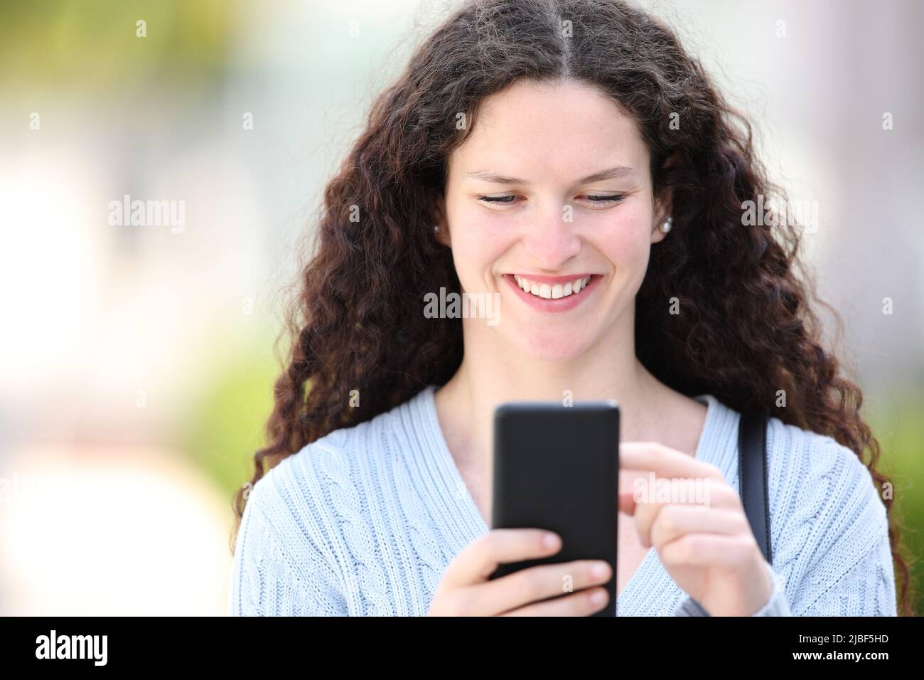 Vorderansicht Porträt einer Frau, die mit dem Telefon auf der Straße unterwegs ist Stockfoto