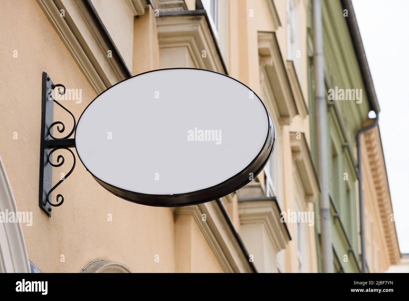 Unbeschriftete ovale Ladenwand aus Metall auf der Straße, die an der Wand befestigt ist. Leeres Plastiktafel-Modell. Stockfoto