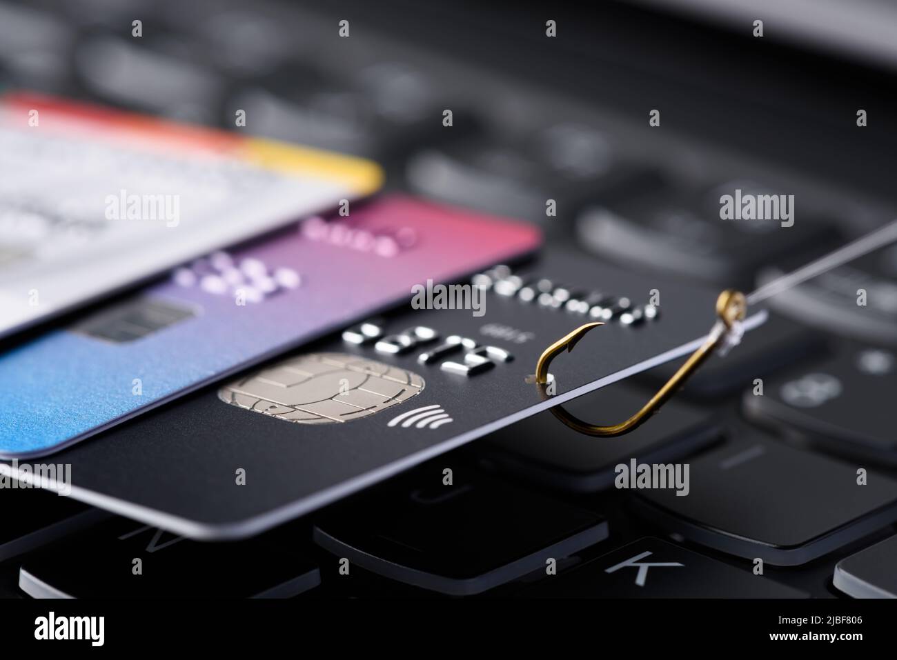Konzept für Phishing-Betrug mit Kreditkarte. Kreditkartendatendiebstahl, Karte auf Angelhaken eingehakt, gezogen aus dem Stapel anderer Karten auf der Tastatur. Stockfoto