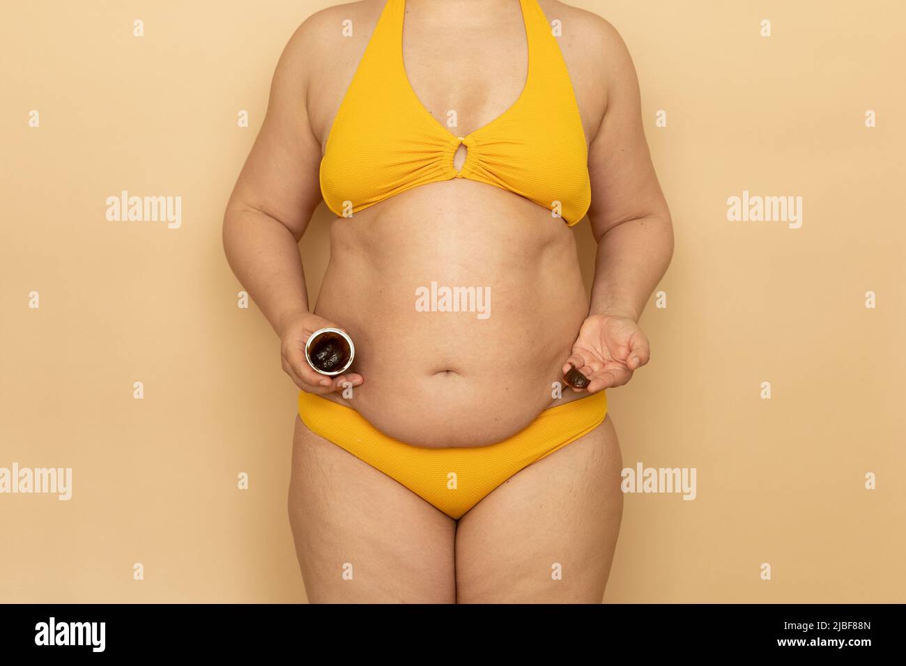 Frau in gelbem Badeanzug mit dicken schlaffe Bauch halten Glas Körpercreme  in der Hand, beige Hintergrund. Abnehmen, Bekämpfung von Übergewicht,  Fettleibigkeit und Stockfotografie - Alamy