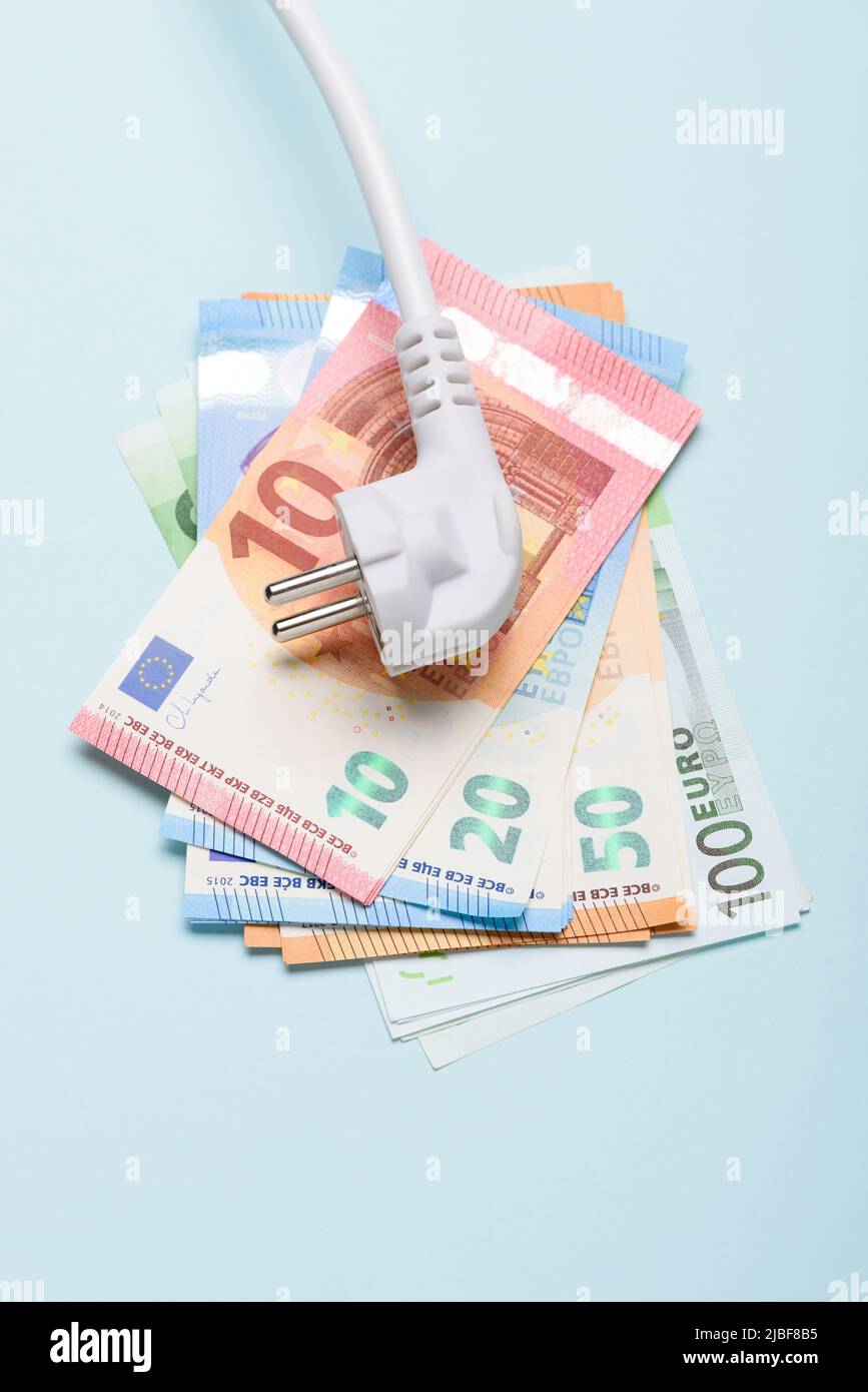 Elektrischer Netzstecker auf Euro-Banknoten auf blauem Hintergrund. Konzept teurer Stromkosten und steigender Energiebillimpreise. Stockfoto
