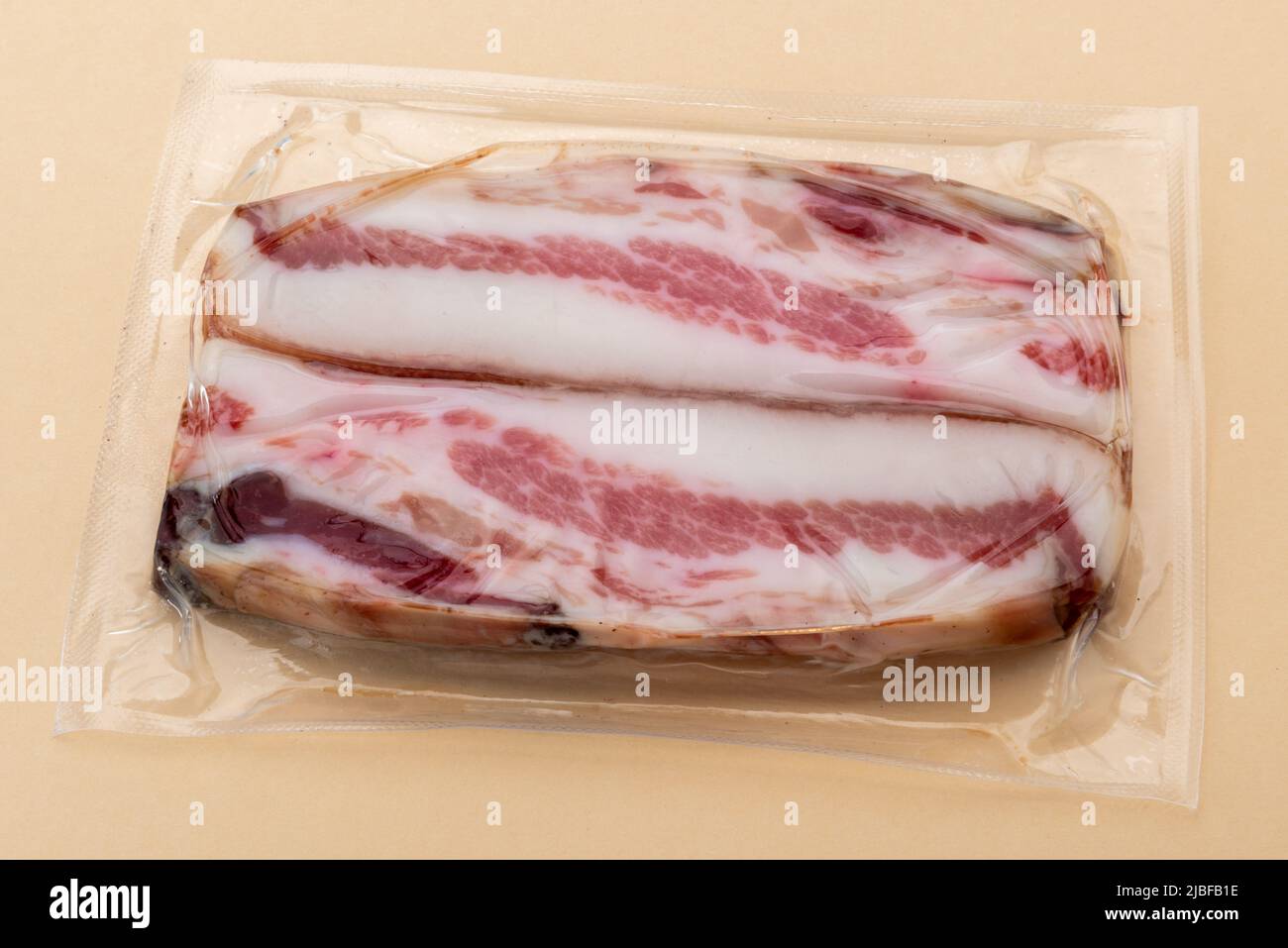 Italienische Guanciale, Scheiben trocken gehärtete Schweinebacke in Vakuum verpackt versiegelt für Sous-Vide-Kochen isoliert auf hellbraunem Hintergrund Stockfoto