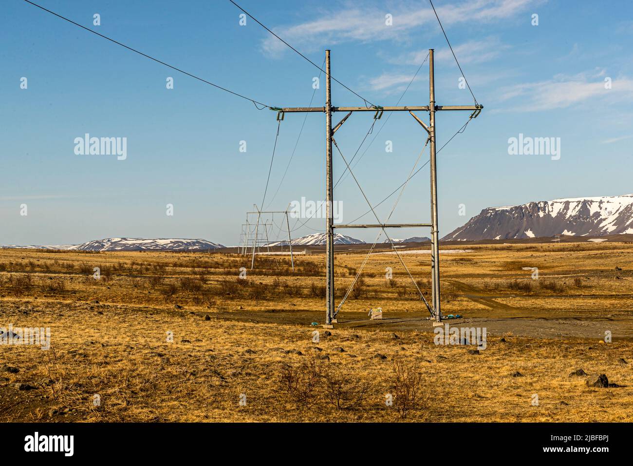 Ein Strommast mit zwei kleiner wirkenden Masten im Hintergrund steht auf einem Plateau nahe dem Mývatn im Norden Islands vor schneebedeckten Tafelbergen im Abendlicht. Die Leitung verläuft durch die Gemeinde Þingeyjarsveit entlang der Kísilvegur-Straße. Stockfoto