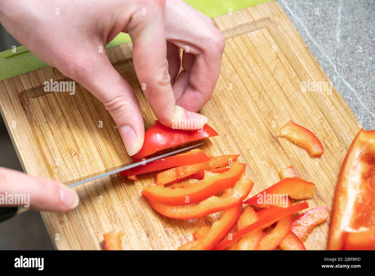 Weibliche Hände schneiden rote saftige rohe Paprika auf einem Brett, Nahaufnahme. Das Konzept des Kochens von hausgemachten Speisen. Salat in der Küche zubereiten. Diät Essen conce Stockfoto