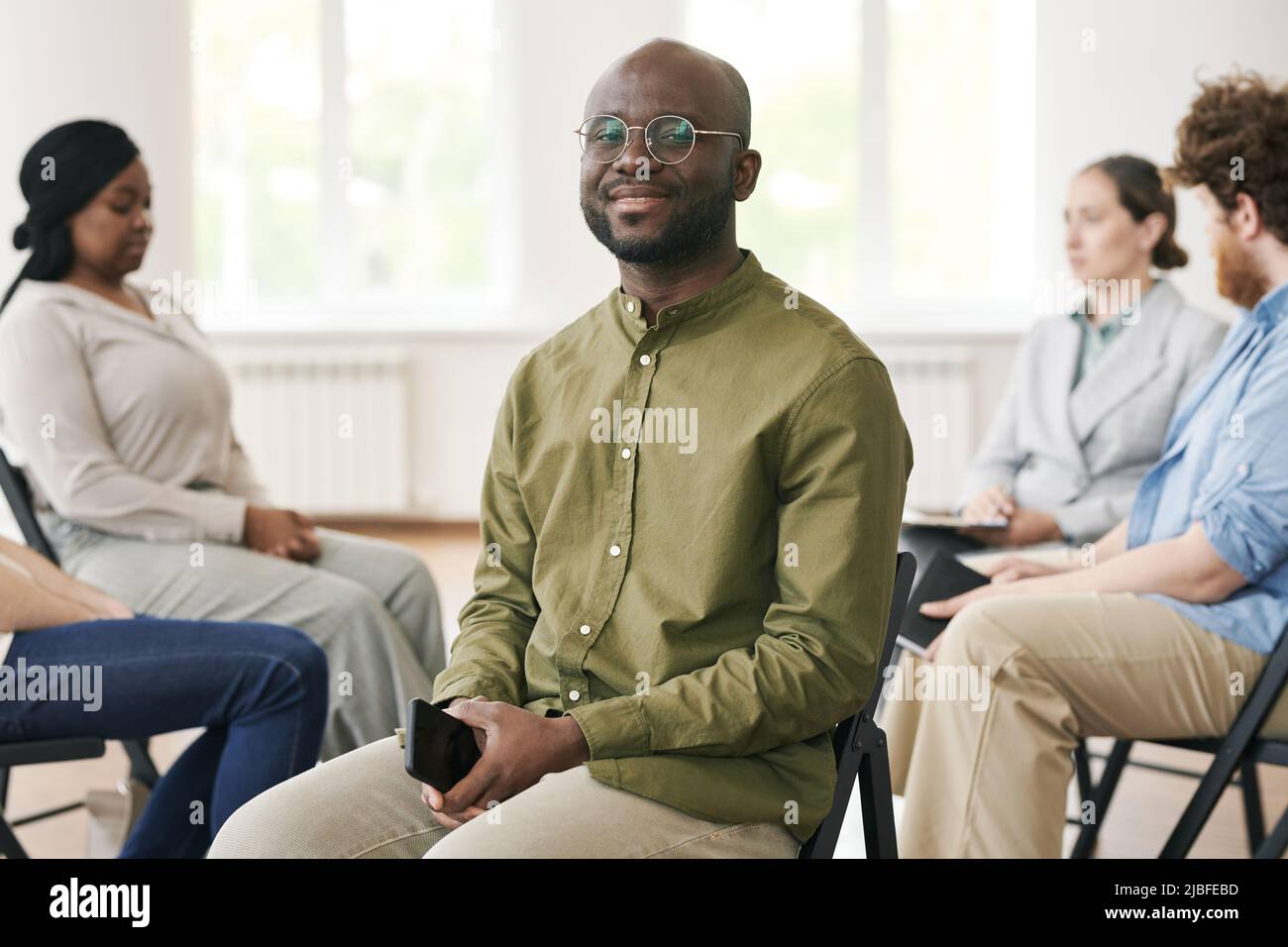 Glücklicher junger schwarzer Mann mit Smartphone sitzt vor den Patienten der Berater Diskussion ihre Probleme während der psychologischen Sitzung Stockfoto