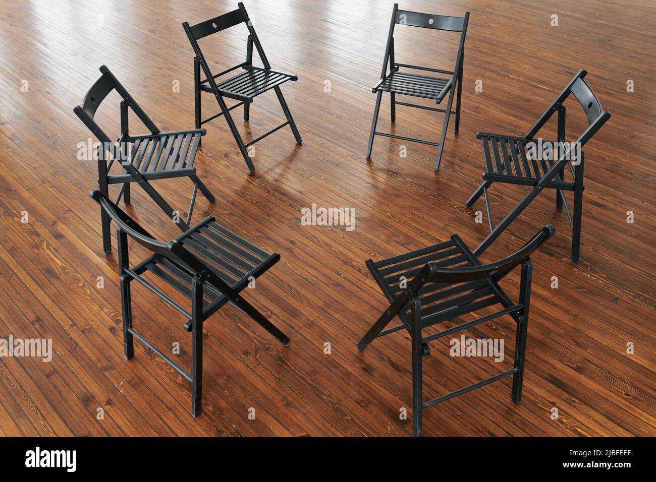 Über dem Winkel von sechs schwarzen Holzstühlen bilden Kreis auf dem braunen Boden des Büros, Hörsaals oder Auditorium für Schulungen und Seminare Stockfoto