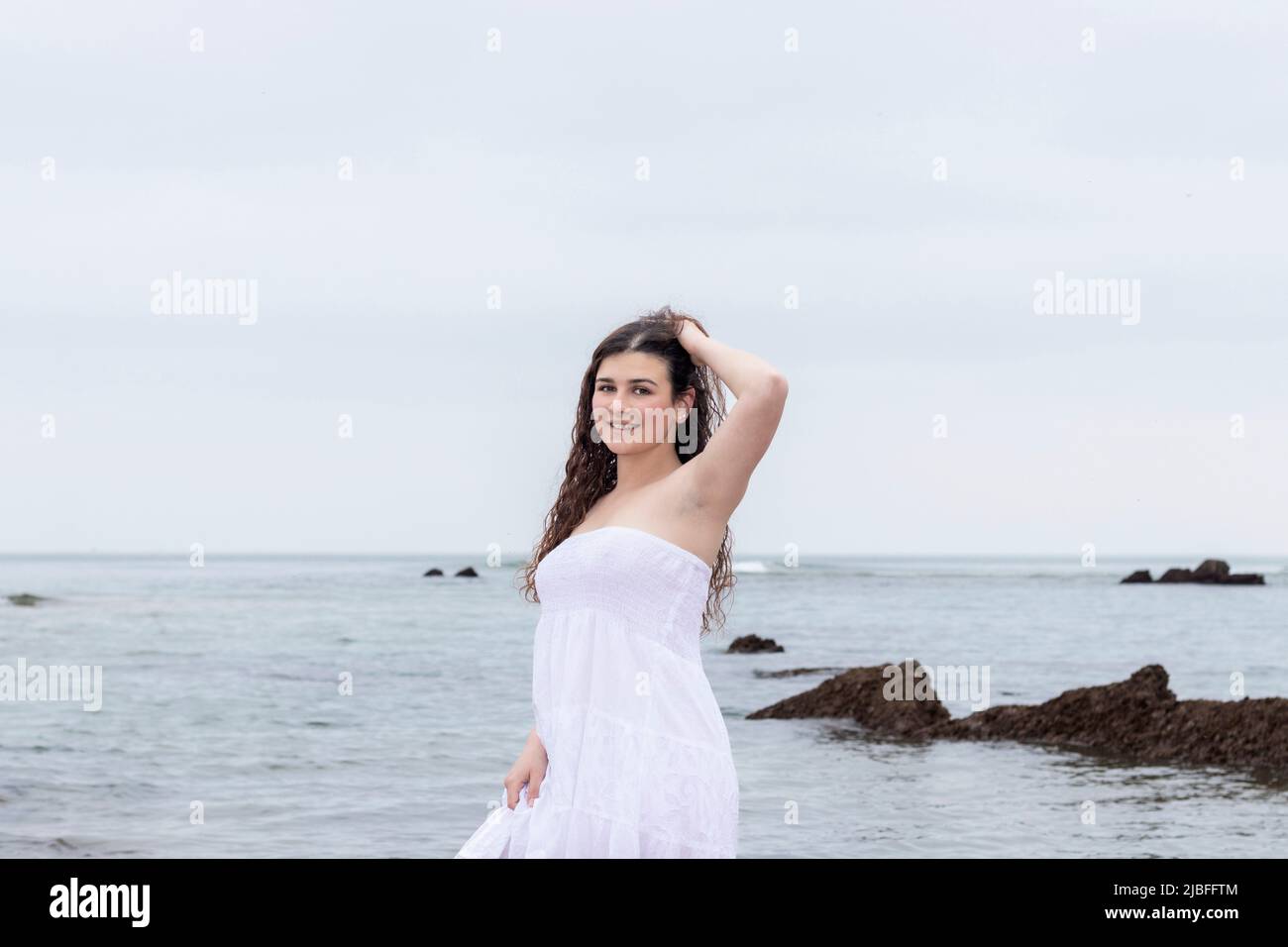 Junge Brünette Frau in weißem Kleid posiert am Meer Stockfoto