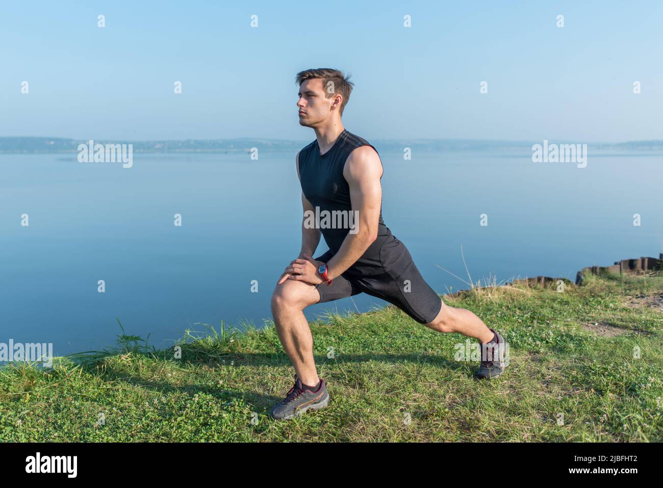 Ein junger, frecher Mann streckt die Beine im Freien und macht einen Ausfallschritt nach vorne Stockfoto