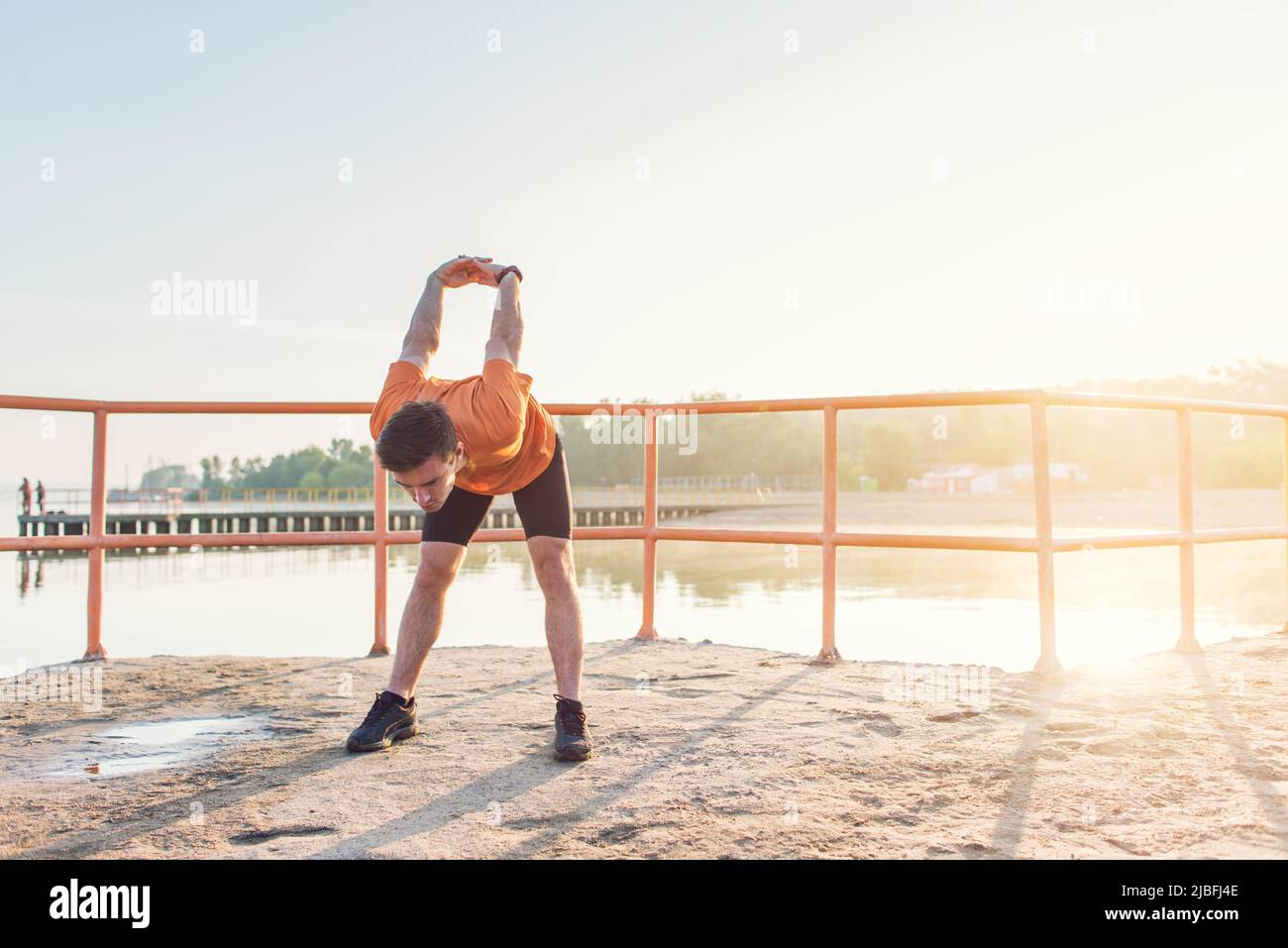 Junger Athlet, der seine Arme hinter dem Rücken hält und sich im Freien dehnt. Stockfoto