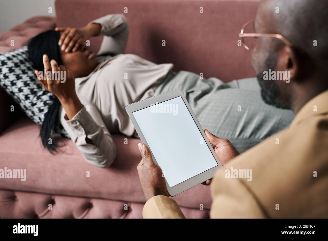 Junge männliche Psychotherapeutin mit Tablet sitzt vor einer weiblichen Patientin, entspannt auf der Couch und beschreibt ihre Sorgen und Probleme Stockfoto