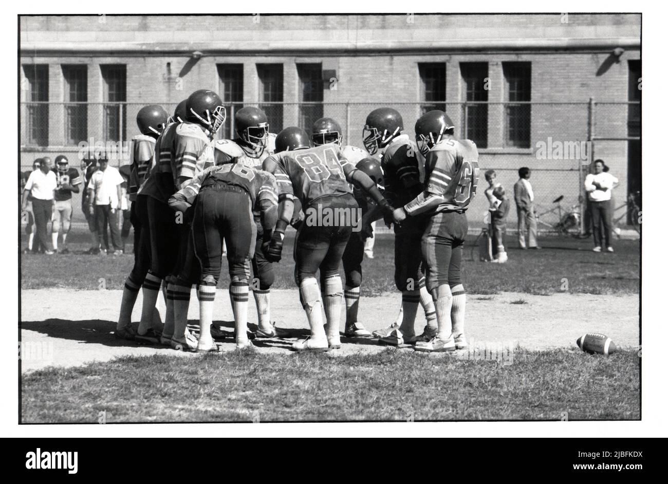 Die Fußballmannschaft der John Jay High School hält Hand in ihrem Gefalle, während das nächste Spiel aufgerufen wird. 1983 in Brooklyn, New York. Stockfoto