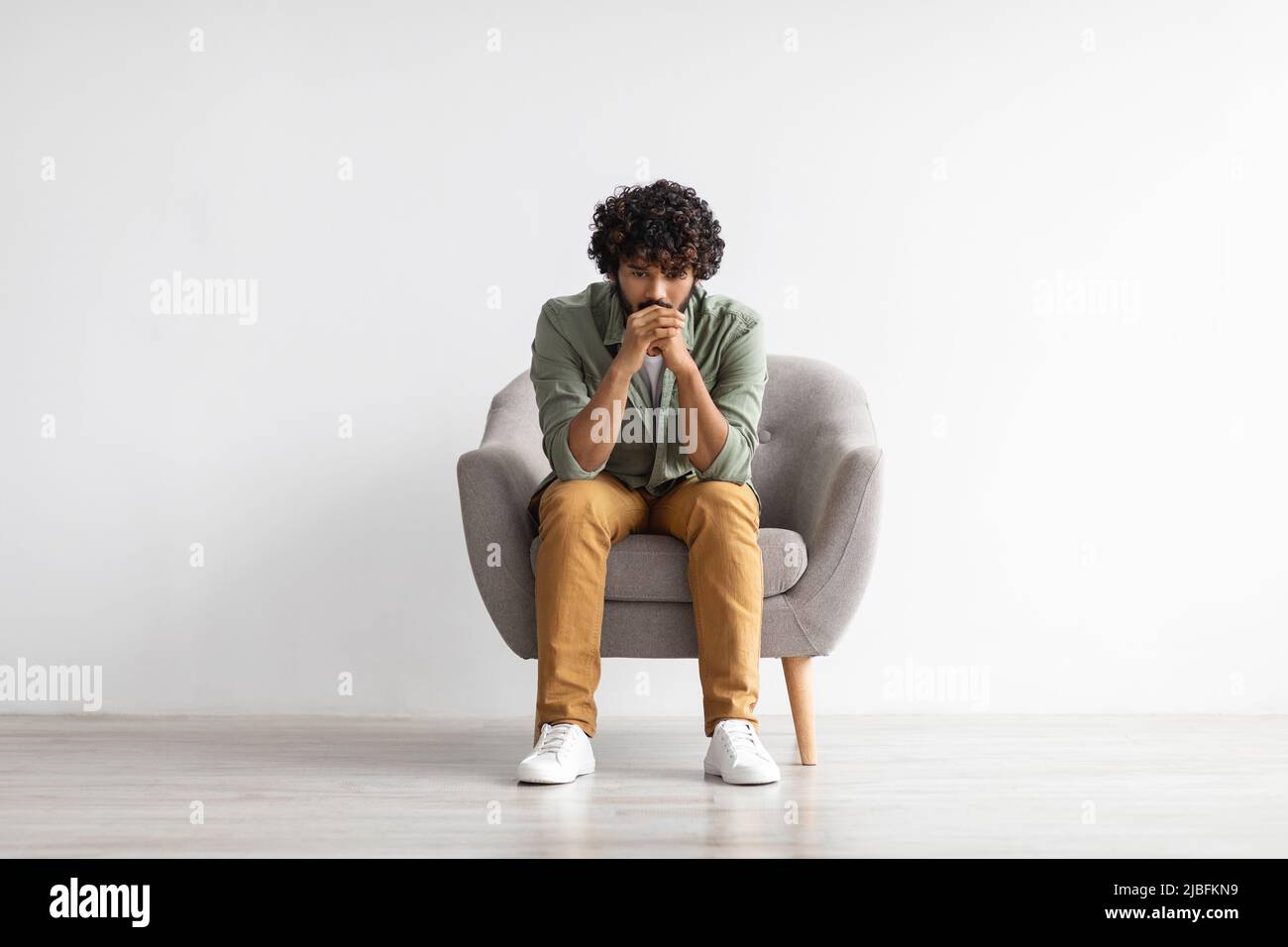 Deprimierter indischer Kerl, der in einem Sessel über Weiß sitzt Stockfoto