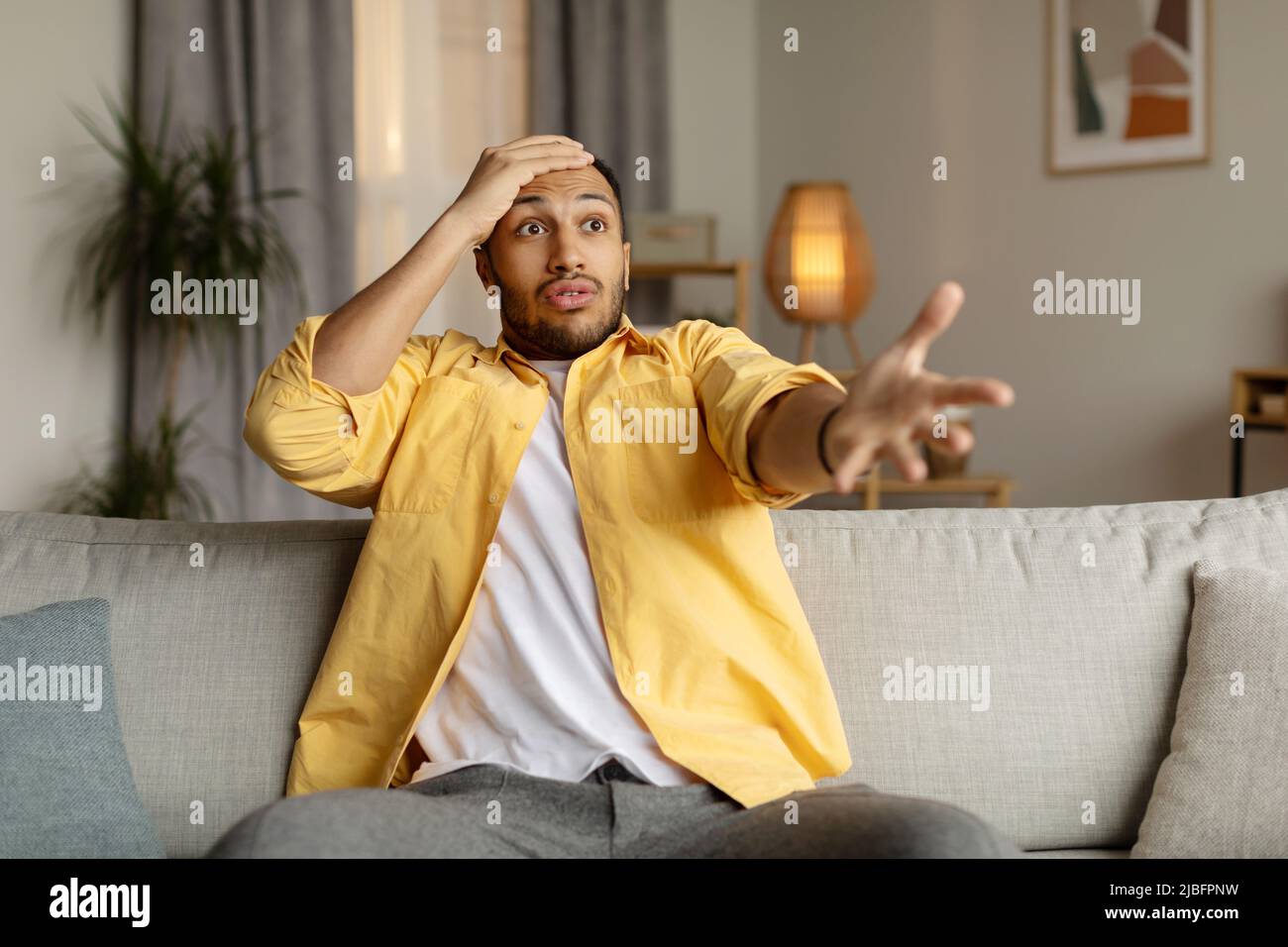Emotionaler junger schwarzer Mann, der Empörung ausdrückt, schockiert durch schlechte Nachrichten oder die Niederlage des Sportteams im Fernsehen zu Hause Stockfoto