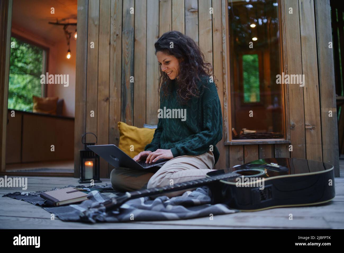 Glückliche junge Frau mit Laptop, die sich im Freien in einem Baumhaus, Wochenendausflug und Remote-Office-Konzept ausruhen lässt Stockfoto