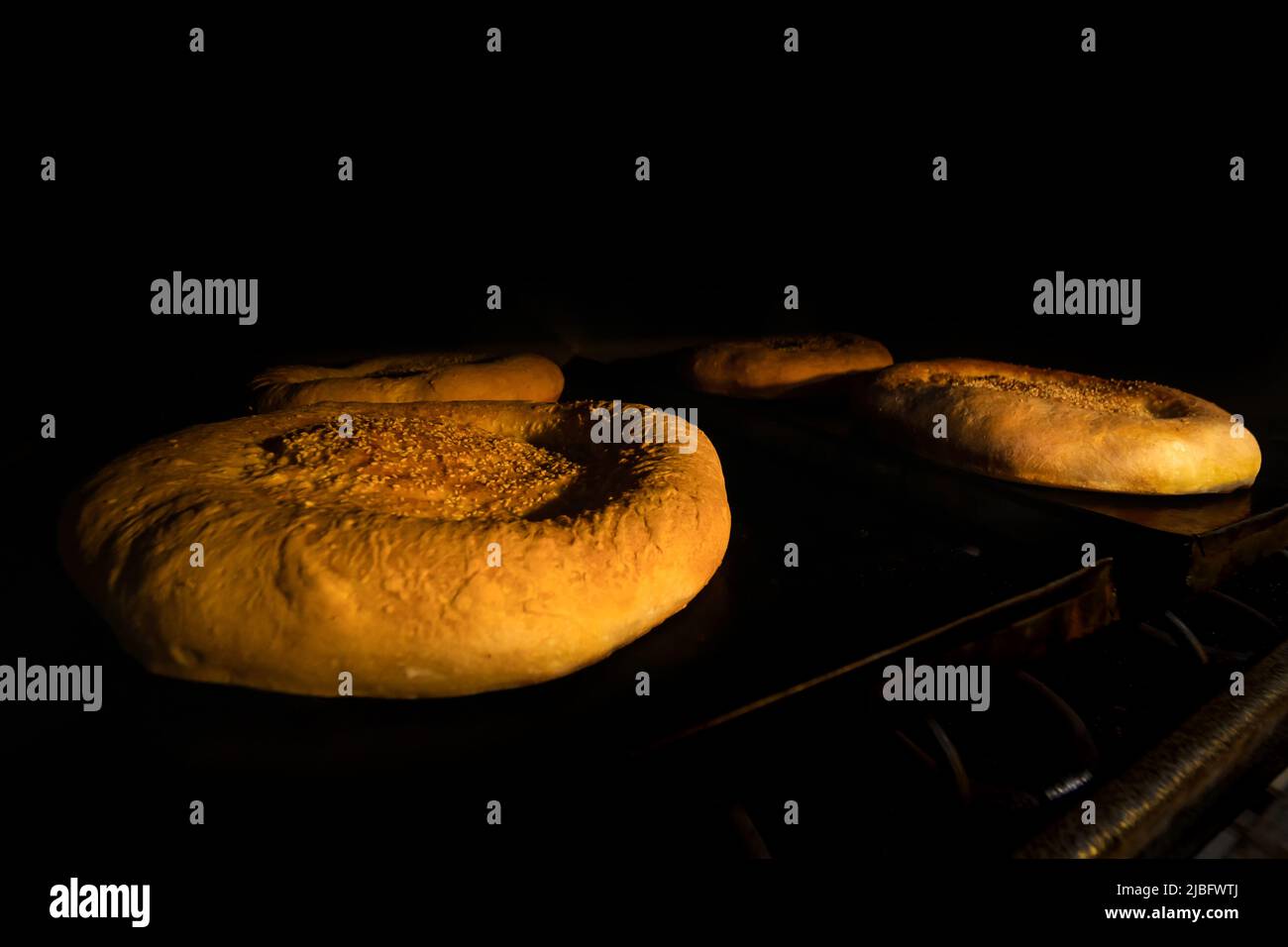 Nahaufnahme von runden Brötchen oder Backwaren mit Sesamsamen in einem elektrischen Produktionsofen Stockfoto