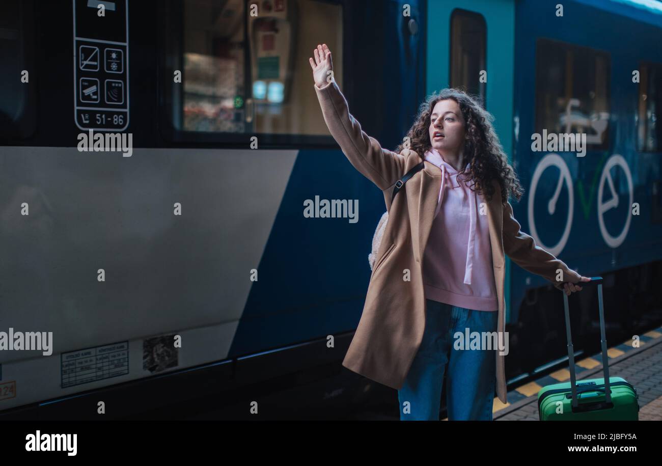 Junge Reisende Frau mit Gepäck stand auf der Plattform und sagte Auf Wiedersehen, winkte jemand im Zug Stockfoto