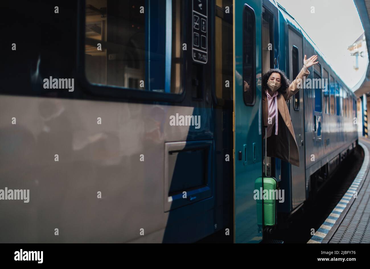 Glückliche junge Reisende Frau mit Gepäck, die am Bahnhofsplatz aus dem Zug aussteigen Stockfoto