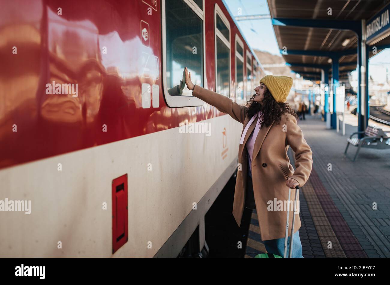 Eine junge Reisende Frau mit Gepäck stand auf der Plattform und sagte Auf Wiedersehen, winkte jemand im Zug Stockfoto