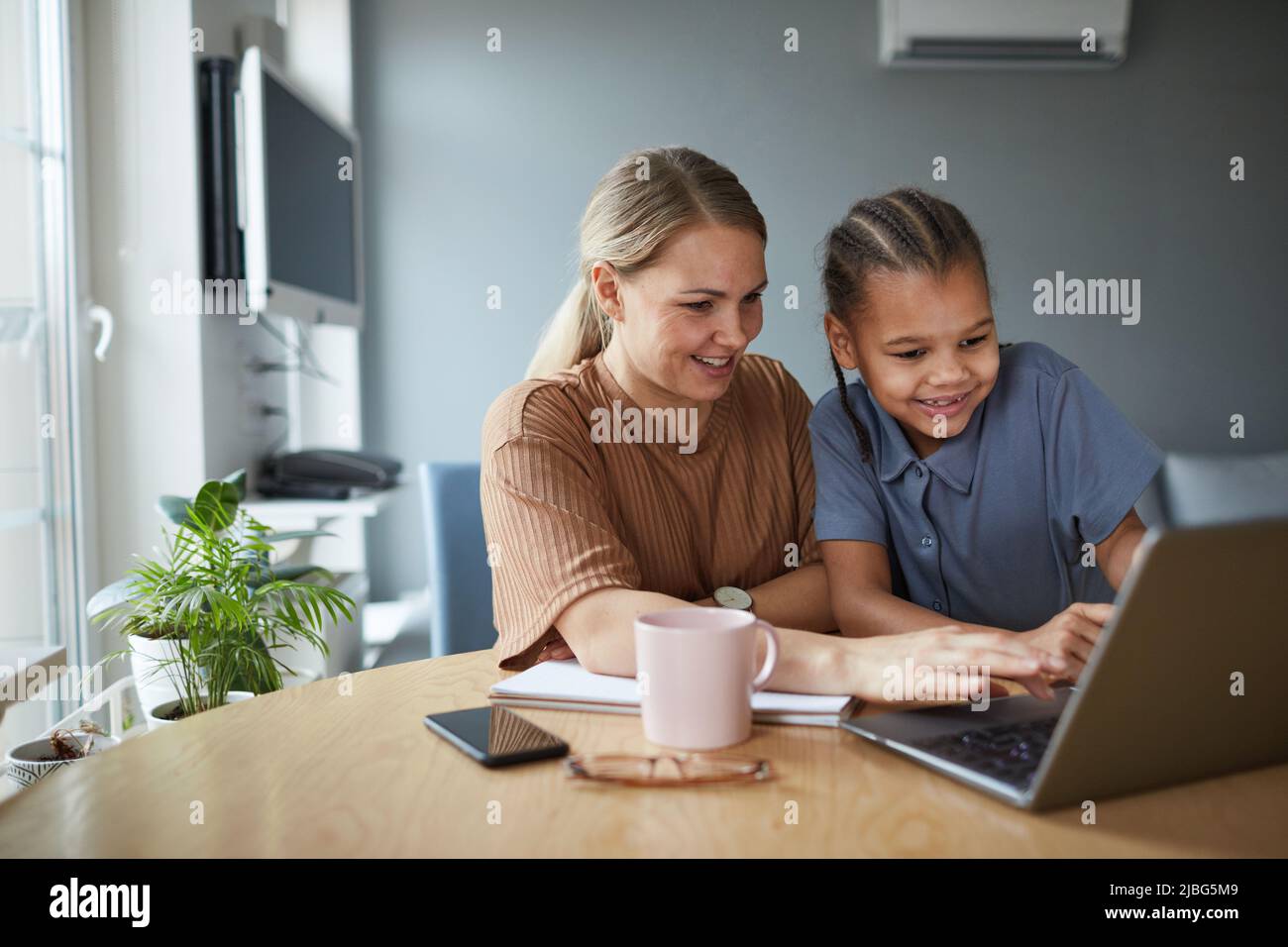 Porträt einer multiethnischen Familie, glücklicher Mutter und Tochter, die beim gemeinsamen Lernen zu Hause auf den Laptop-Bildschirm blicken und Platz kopieren Stockfoto