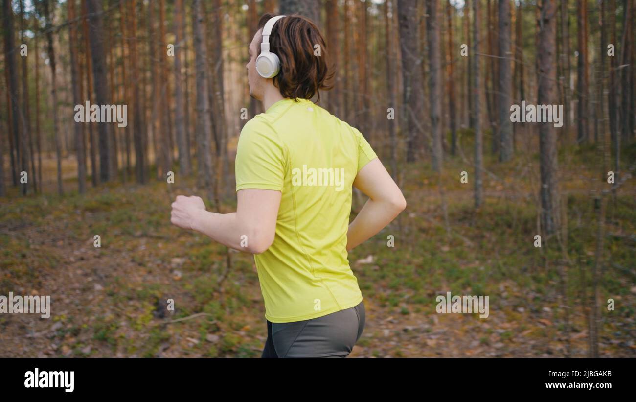 Junger Mann mit weißen kabellosen Kopfhörern läuft durch Kiefernwald. Läufer hören beim Ausdauertraining im Freien Musik Stockfoto