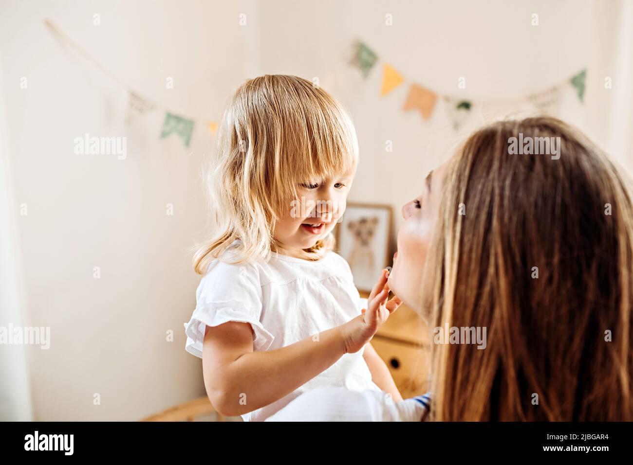 Ein kleines Kind sieht und berührt das Gesicht seiner Mutter. Mama lehrt kleine Tochter, sich um die Gesichtshaut zu kümmern Stockfoto