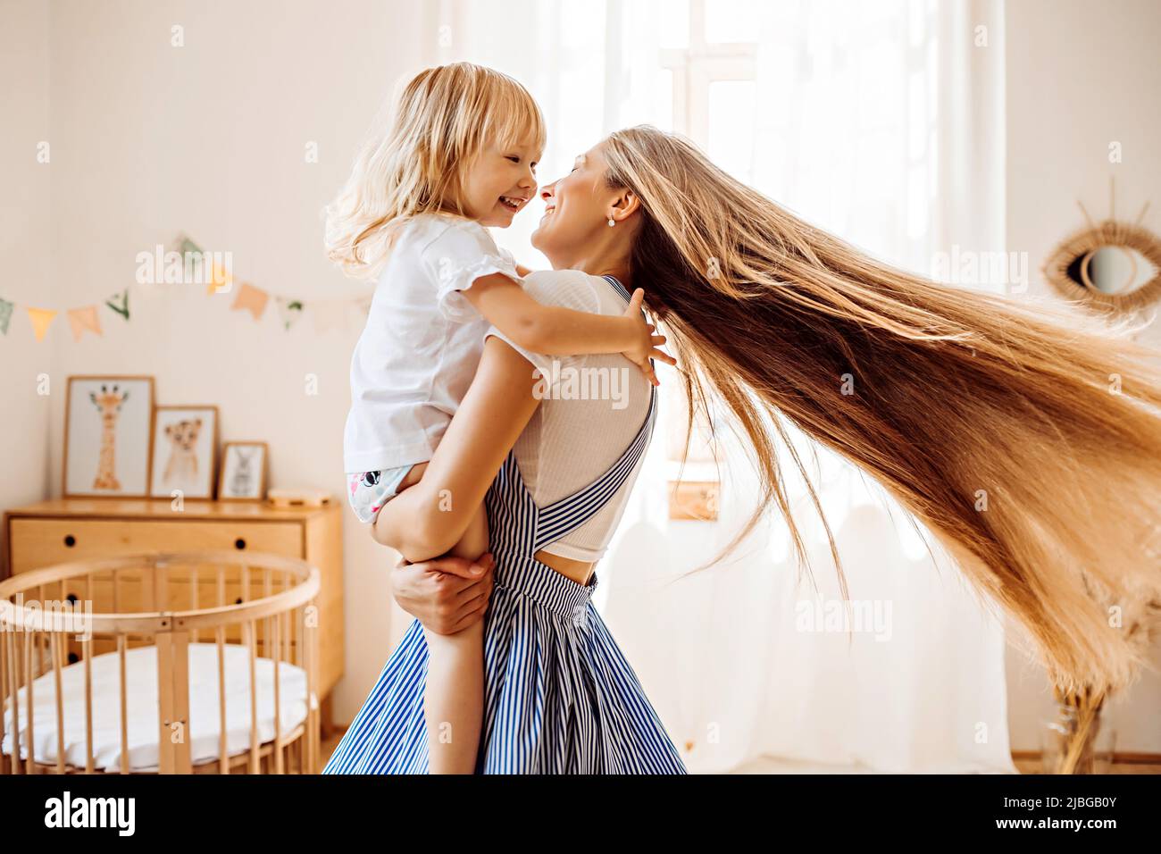 Junge Mutter oder Babysitter mit einem kleinen Mädchen in ihr Die Arme drehen sich in der Mitte des Raumes Stockfoto