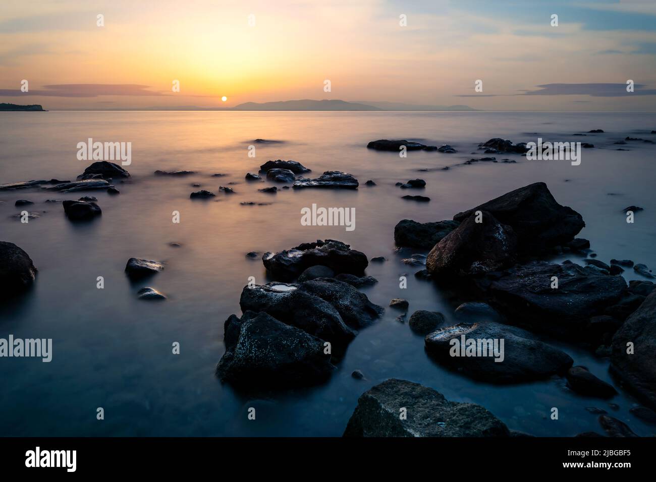 Langzeitaufnahme von Meer, Felsen und Sonnenuntergang. Konzept von Entspannung, Ruhe, Ruhe und innerer Ruhe. Stockfoto