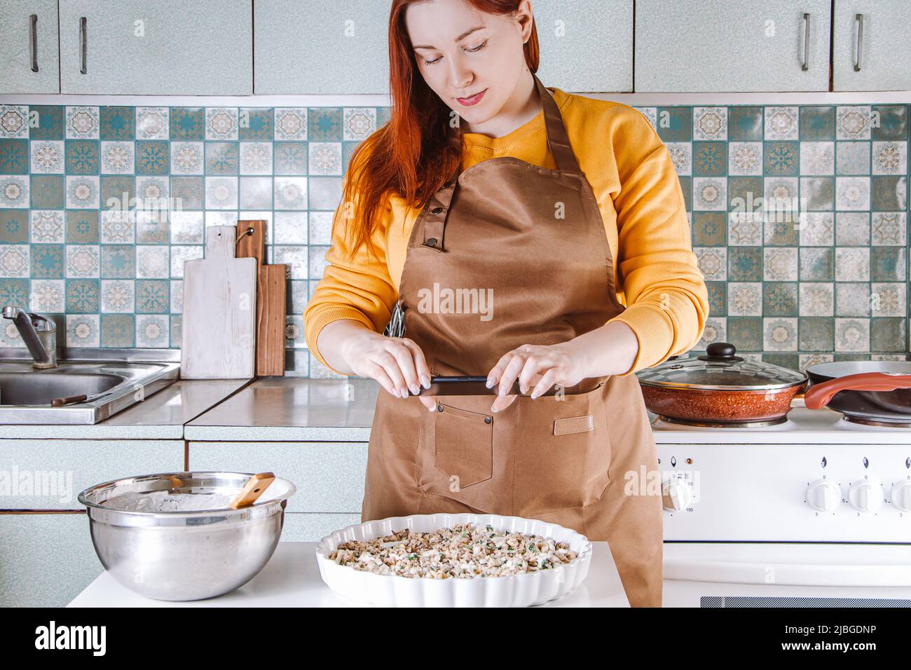 Junge Frau kocht in der heimischen Küche und fotografiert Lebensmittel für soziale Medien. Blogger schreibt einen kulinarischen Blog. Lifestyle, Home-Leisure-Konzept. Stockfoto