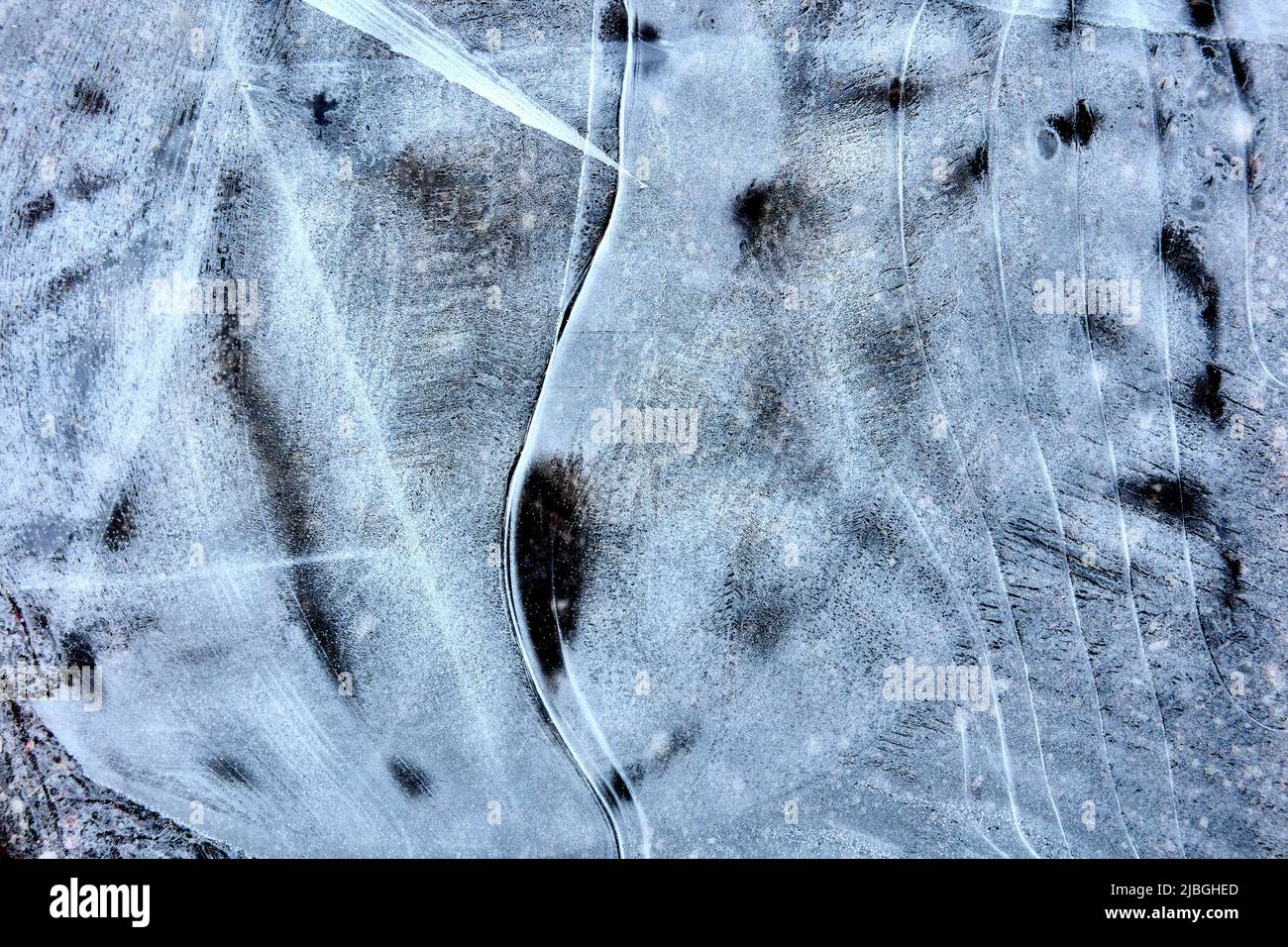 Schwarze und weiße Eisstruktur auf der Oberfläche der gefrorenen Pfütze. Stockfoto
