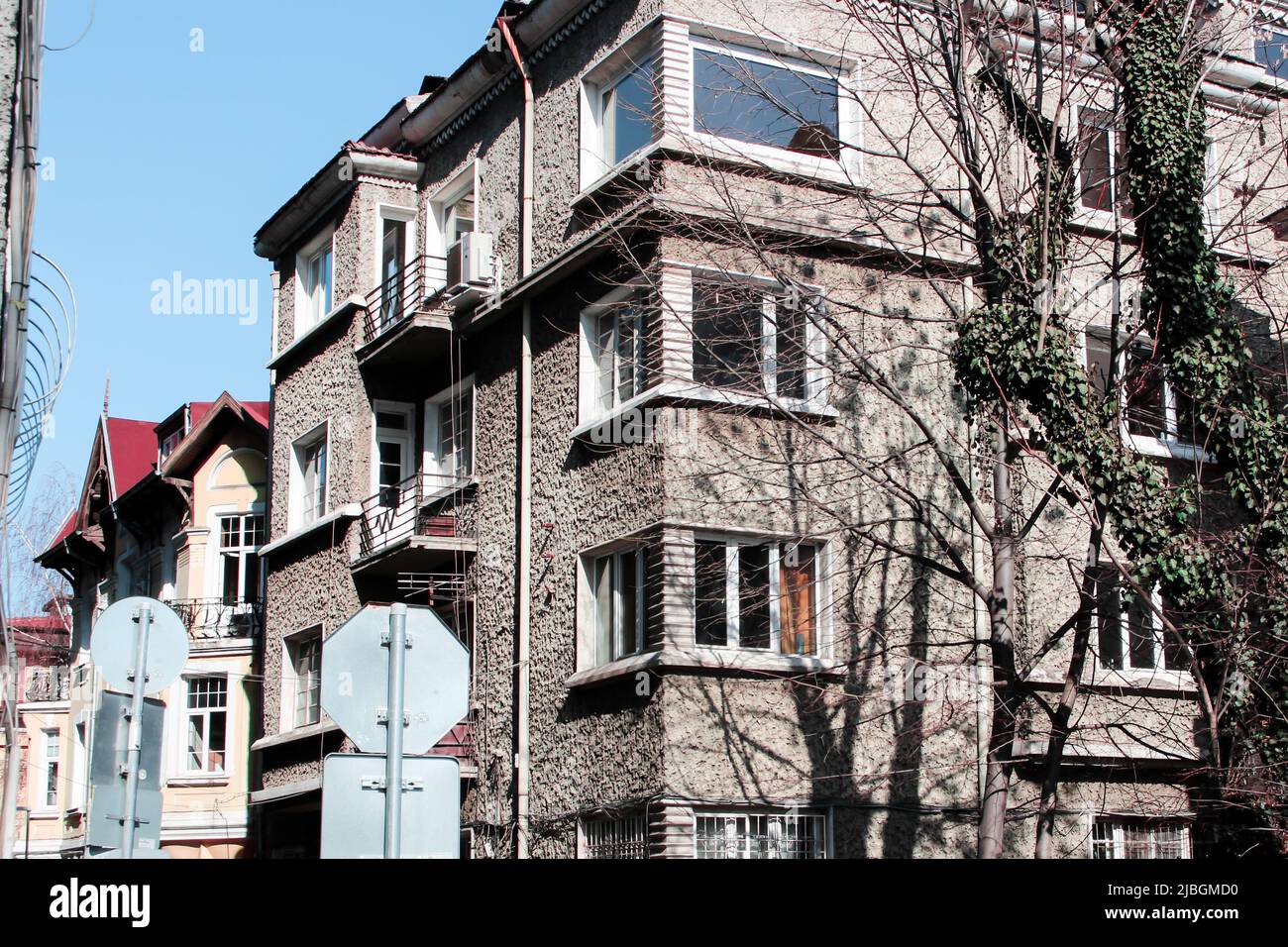 Alte europäische Wohnung mit rauer Oberfläche. Es gibt Bäume und Straßenschilder im Bild. Stockfoto