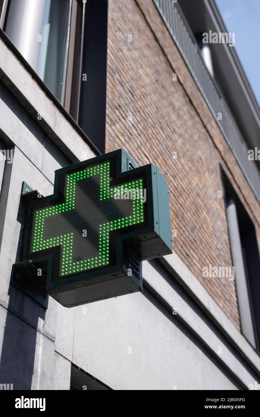 Schild mit beleuchtetem grünen Kreuz, Anzeige für eine Apotheke. Ein erkennbares grünes dynamisches Apothekerkreuz an der Fassade in Maastricht Stockfoto