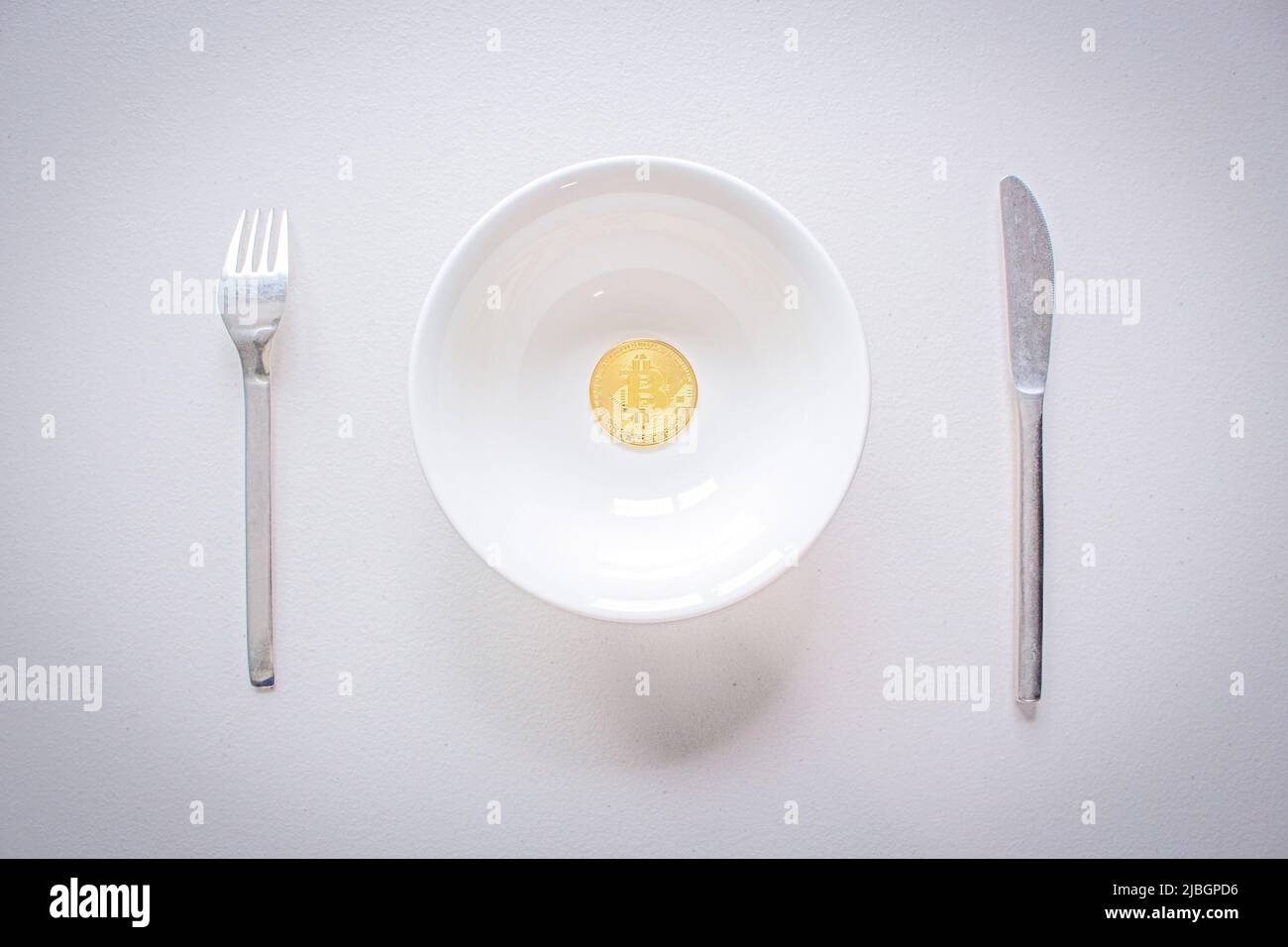 Konzeptbild der Bitcoin-Hartgabel (Blockkette). Goldenes Bitcoin auf dem Teller mit Gabel und Messer. Kryptowährung Münze auf weißem Tisch serviert. Stockfoto
