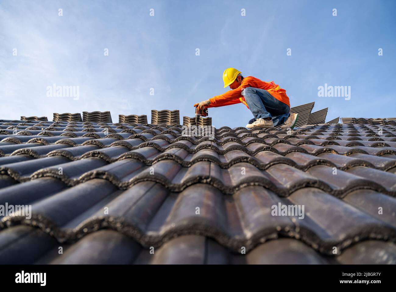 Ein Bauarbeiter installiert ein neues Dach, ein Elektrobohrer wird auf neuen Dächern mit Betondachziegeln und Dachwerkzeugen verwendet. Stockfoto