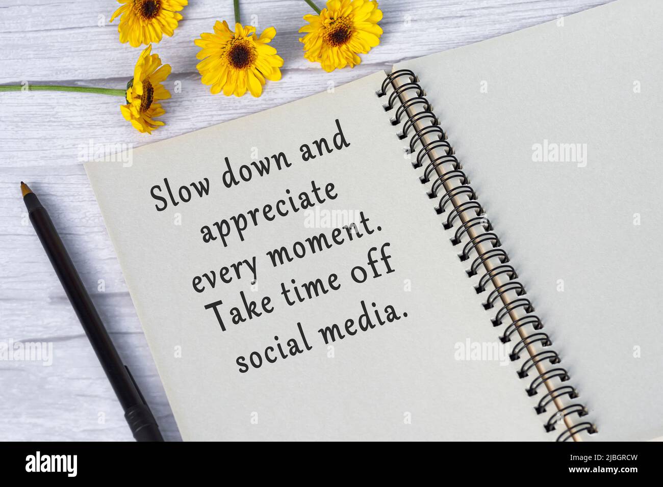 Motivationszitat auf Notizbuch mit Sonnenblumen auf Holzschreibtisch - verlangsamen und schätzen Sie jeden Moment, nehmen Sie sich Zeit von den sozialen Medien. Stockfoto