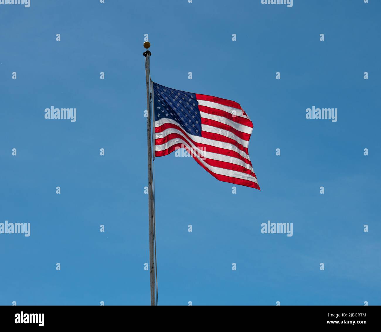 Eine leuchtend rot-weiße und blaue amerikanische Flagge, die in einem klaren blauen Himmel vor Hintergrund winkt Stockfoto