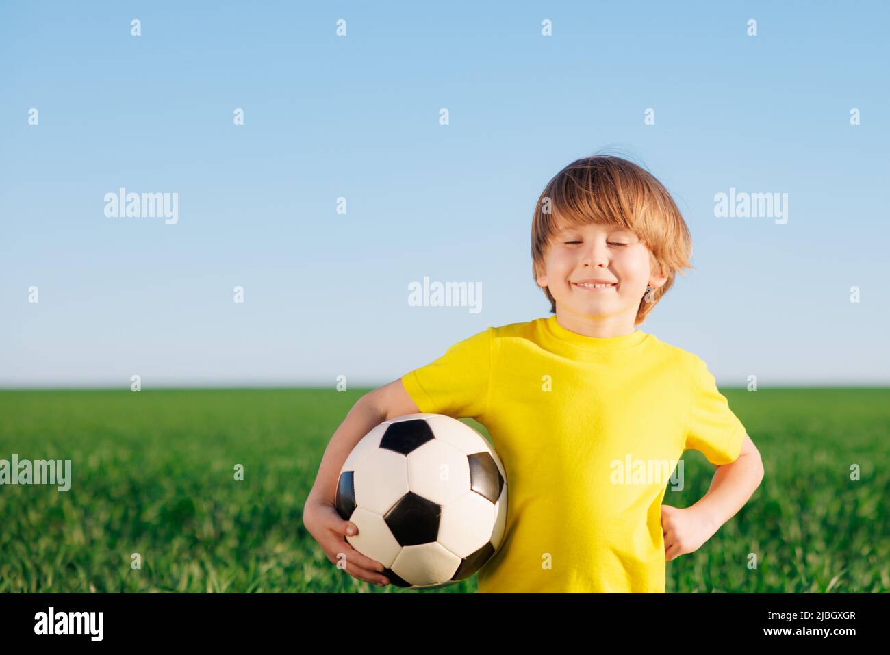 Glückliches Kind gibt vor, ein Fußballspieler zu sein. Porträt eines Kindes im Freien. Junge gegen grünes Feld. Erfolg und Siegerkonzept Stockfoto
