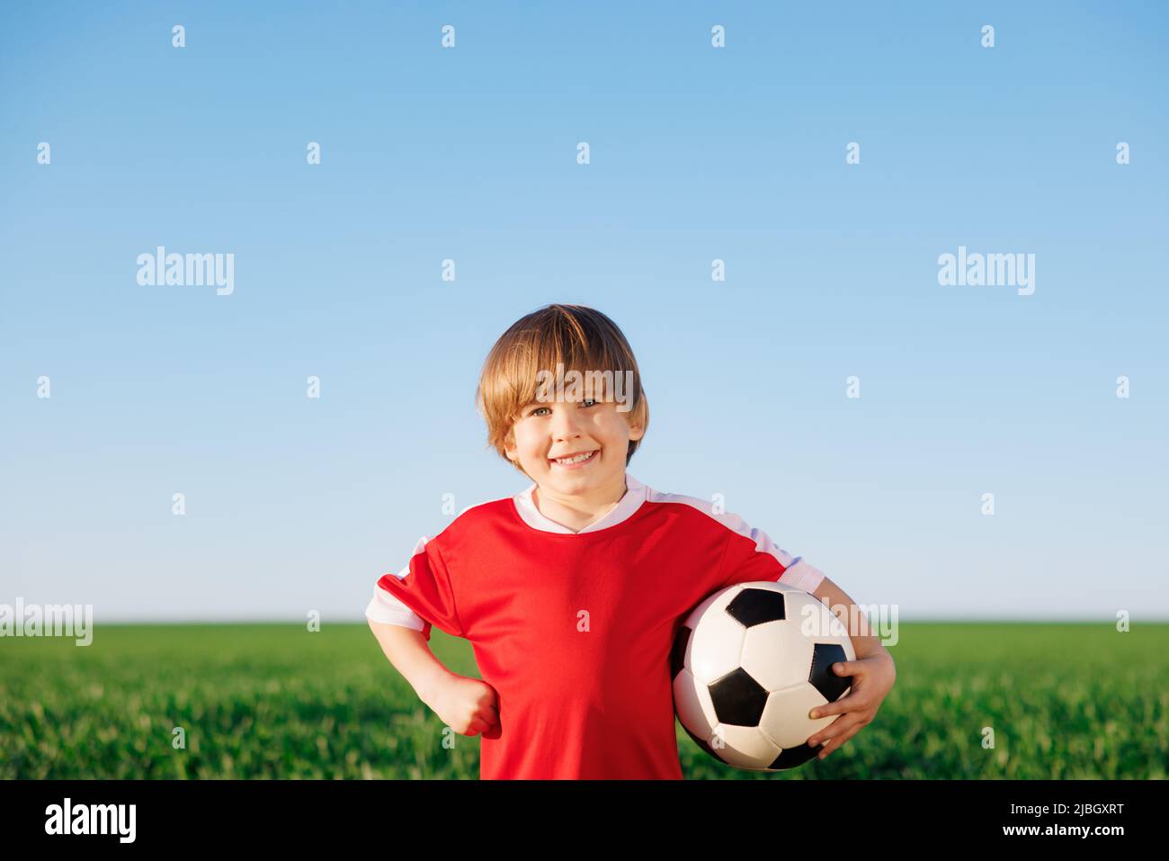 Glückliches Kind gibt vor, ein Fußballspieler zu sein. Porträt eines Kindes im Freien. Junge gegen grünes Feld. Erfolg und Siegerkonzept Stockfoto