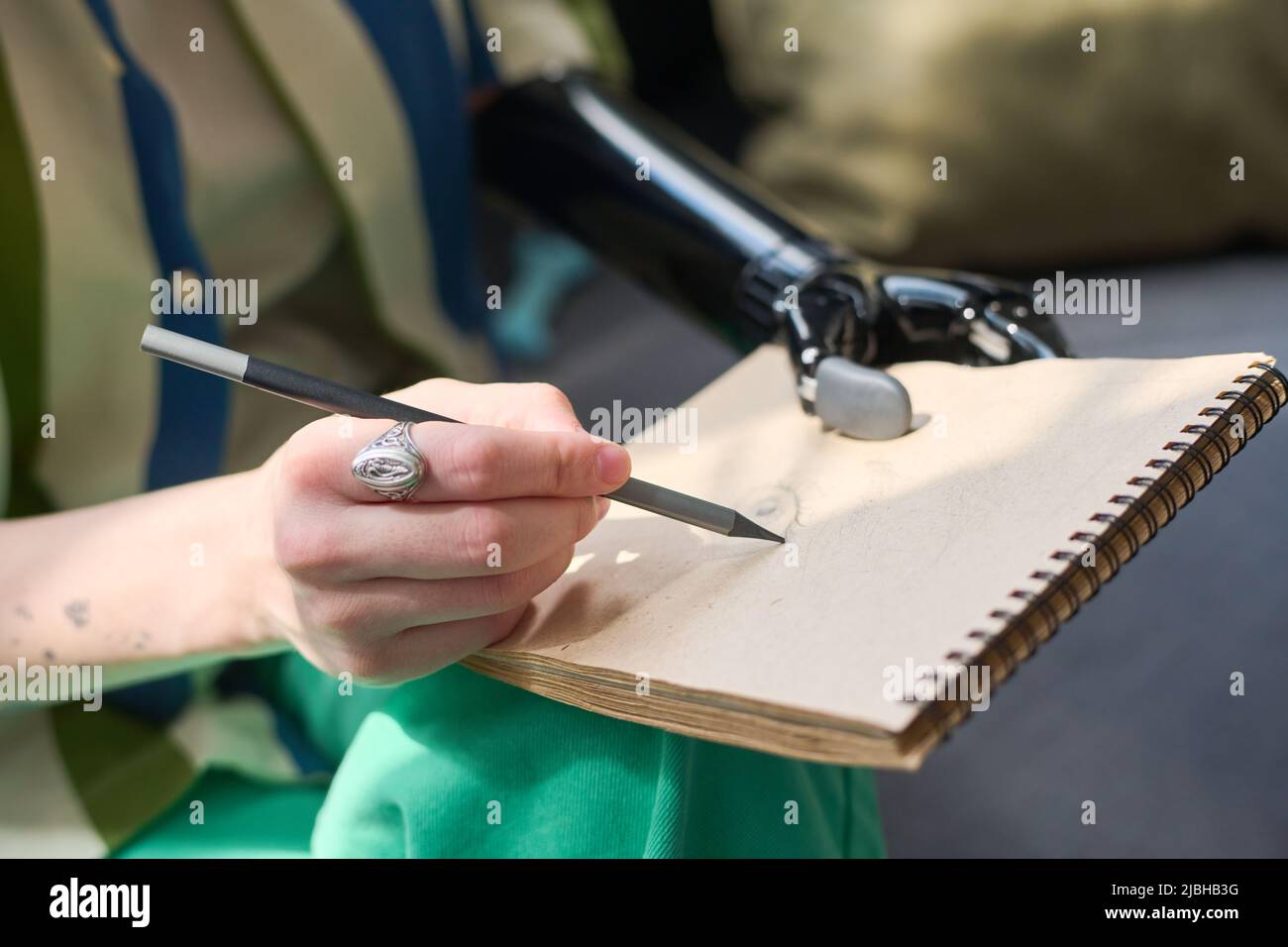 Hand einer jungen Frau mit körperlicher Behinderung, die Bleistift über eine leere Seite des Notizblocks hält, während sie auf dem Sofa sitzt und Skizze zeichnet Stockfoto