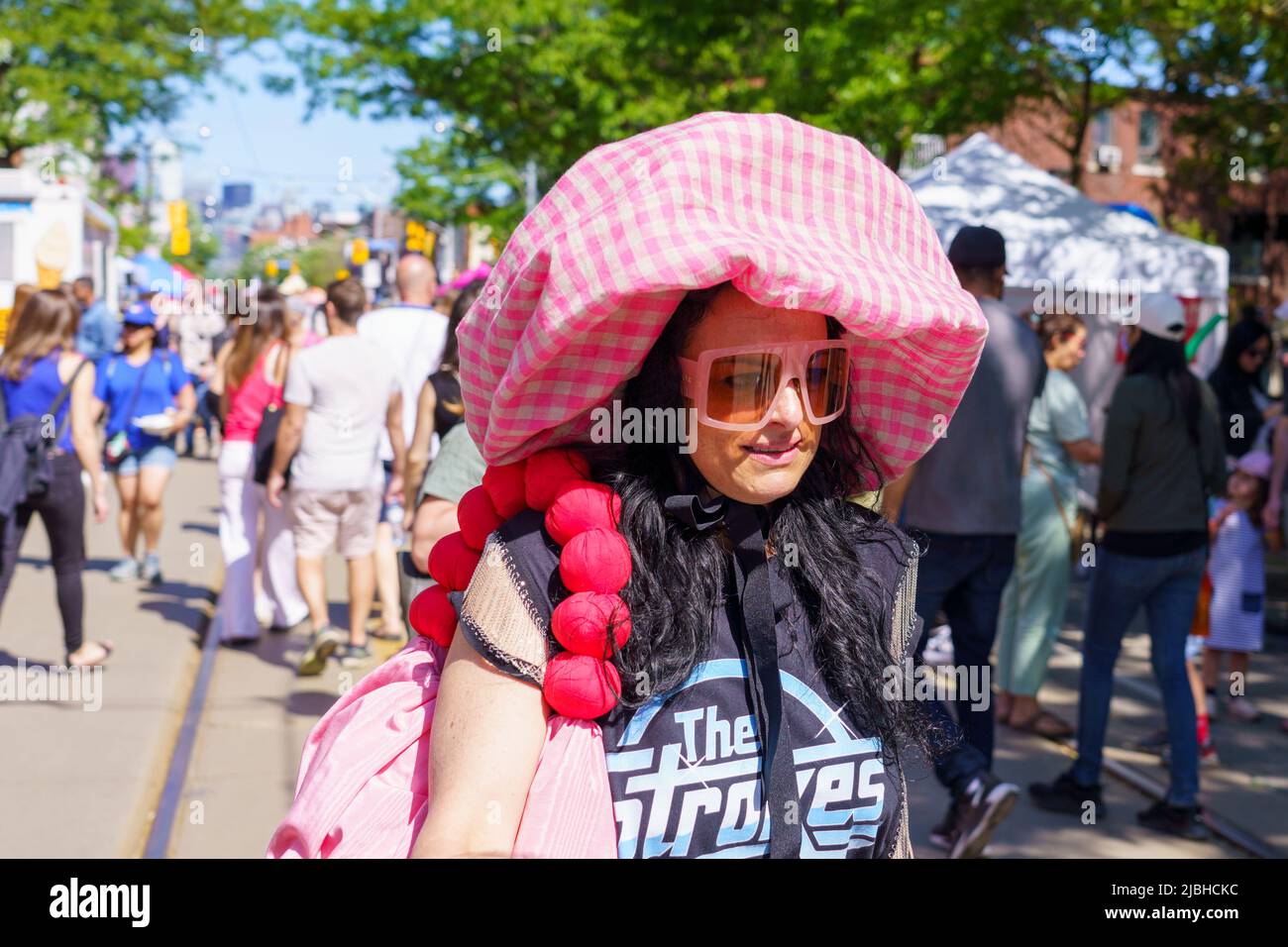 Eine Frau mit einem großen Stoffhut geht während des Do West Festivals in Dundas St. West. Andere zufällige Personen sind in der Szene. Stockfoto