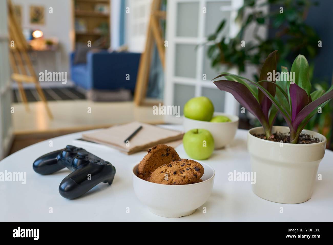 Gruppe von häuslichen Objekten auf weißem Tisch im Wohnzimmer gegen ein anderes Zimmer mit blauer Couch in großen modernen Wohnung Stockfoto